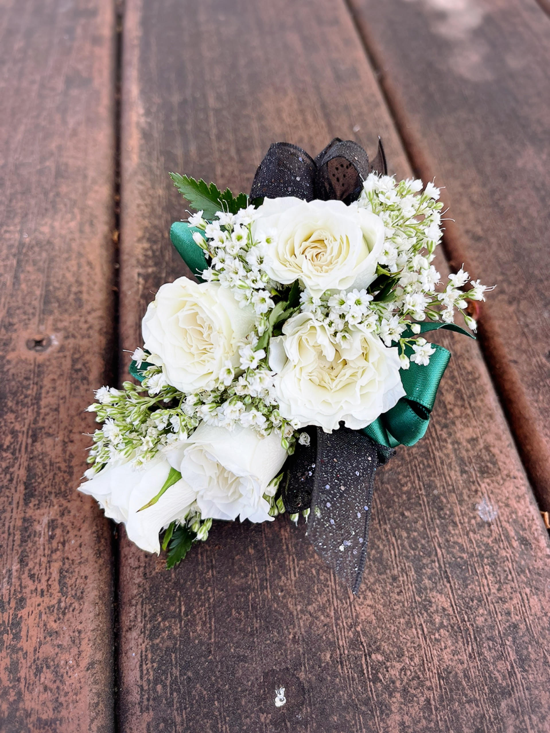 White rose boutonniere with black and green ribbon on wood