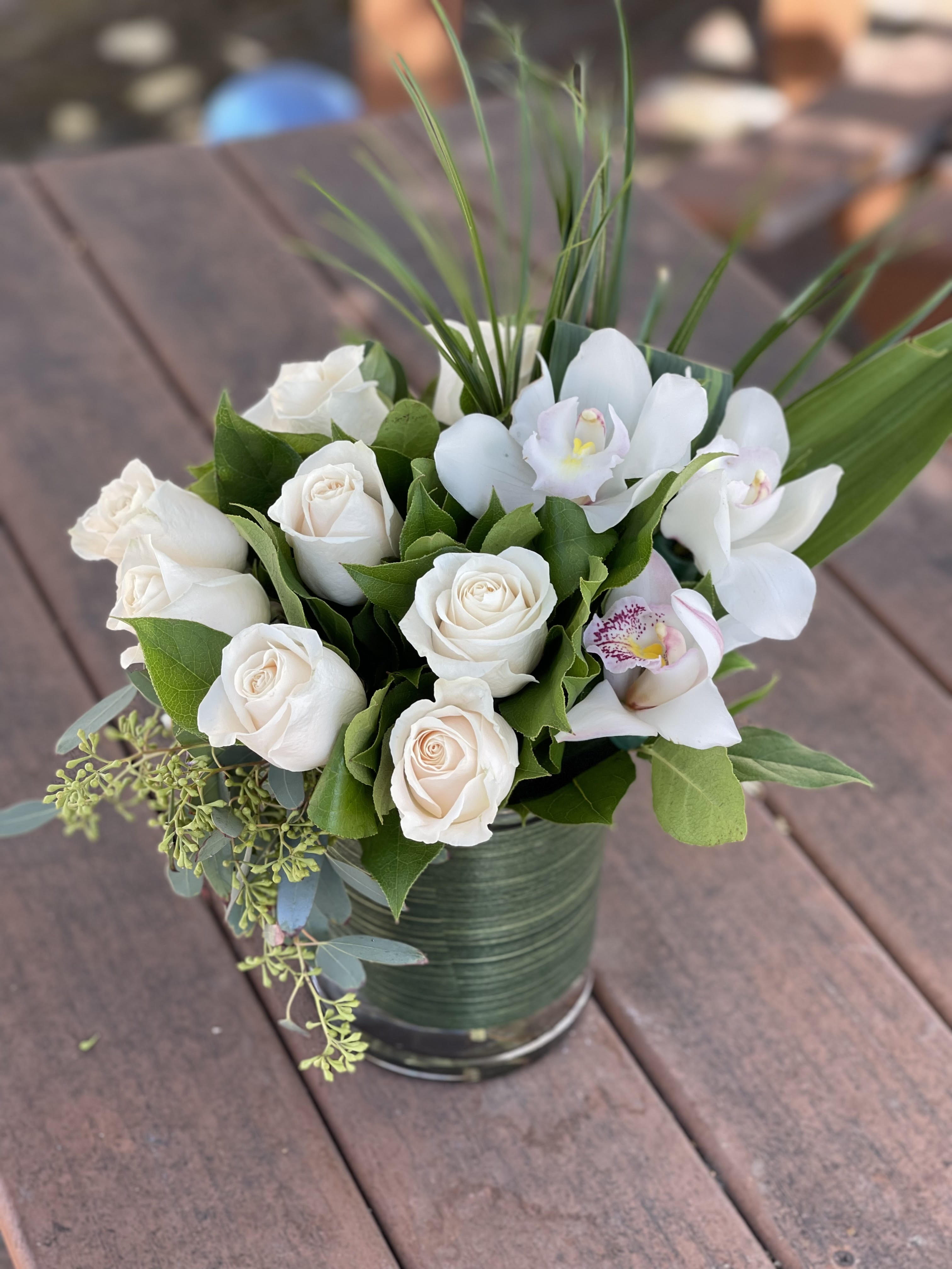 White roses and orchids arranged in a green tin container