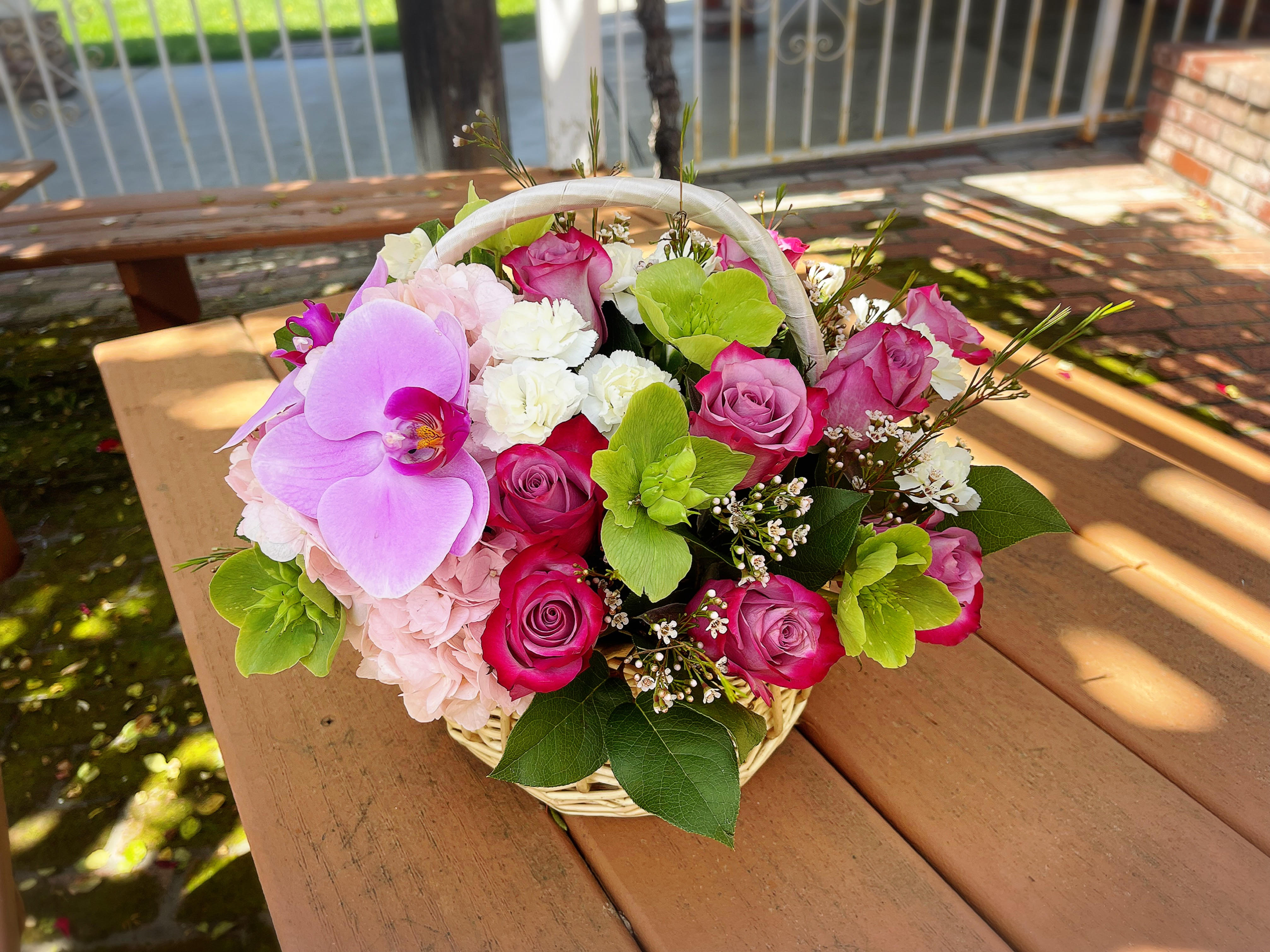 Basket arrangement of pink roses, orchids, hydrangea, and white carnations