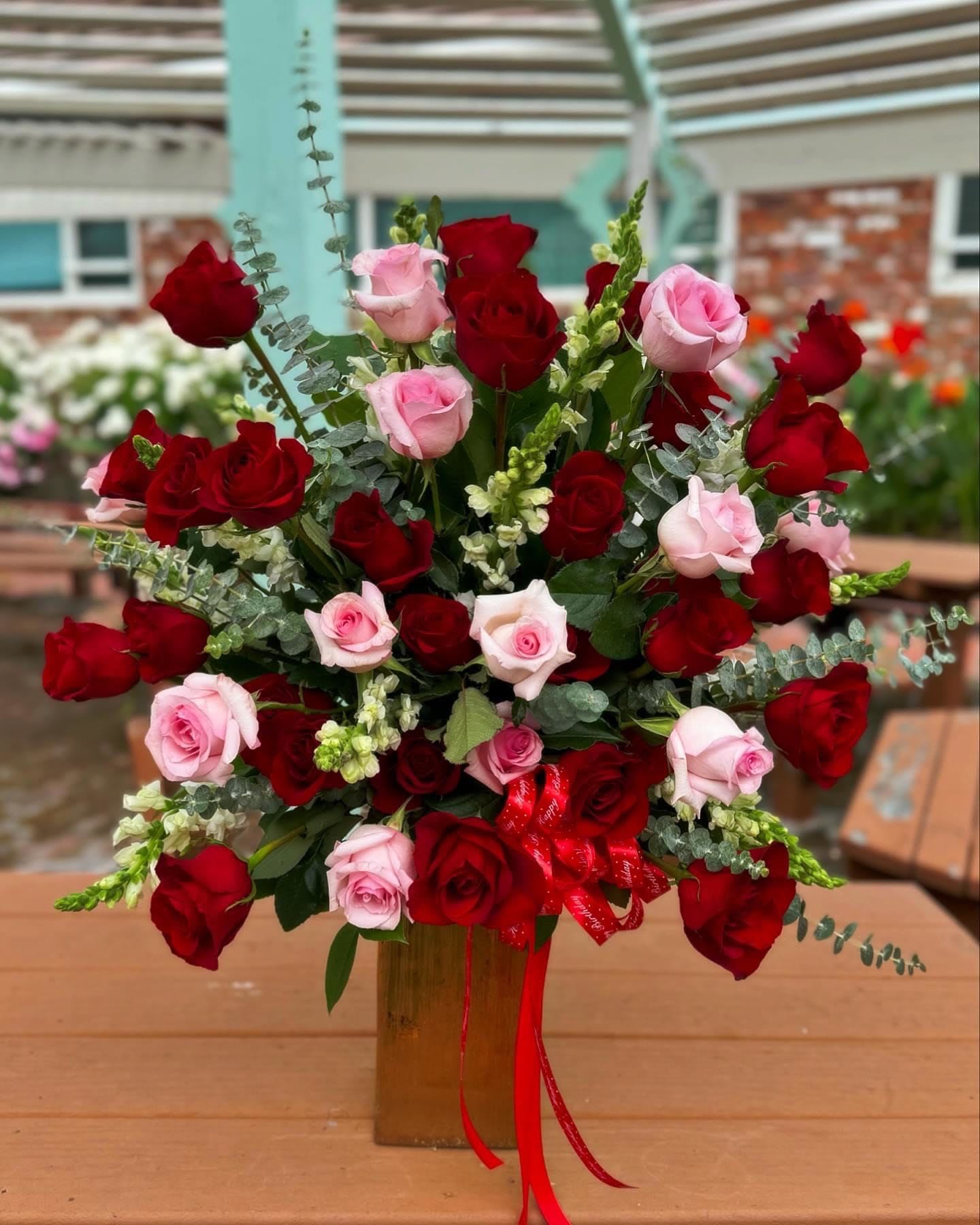Red and pink roses arranged in a tall vase with ribbon