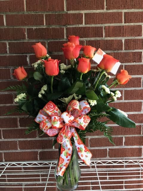 Orange rose bouquet in a glass vase with a patterned ribbon
