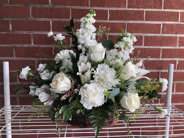 White floral arrangement in a wicker basket with roses and lilies