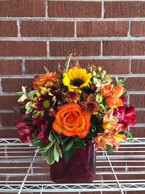 Mixed bouquet with orange roses and a sunflower in a burgundy vase