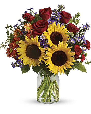 Bouquet of sunflowers, red roses, and purple flowers in a glass vase
