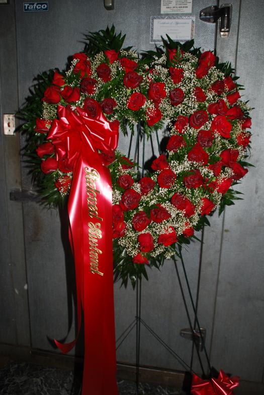 Heart-shaped red rose wreath on a stand with a red ribbon