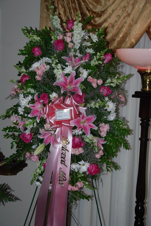 Tall standing floral spray with pink lilies and roses on a ribboned easel