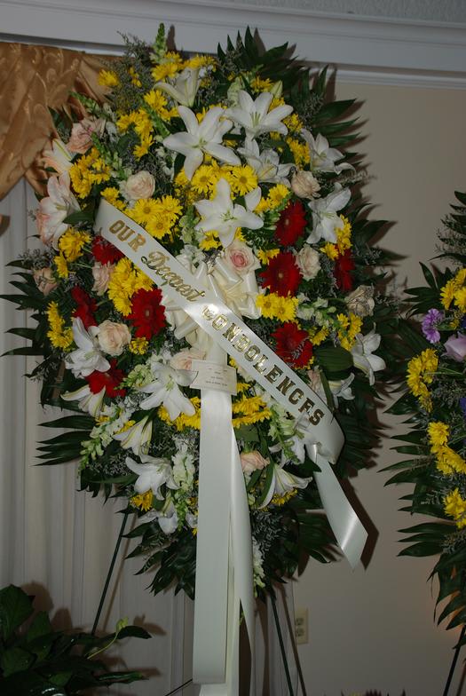 Large funeral wreath with white lilies, yellow daisies, and red flowers