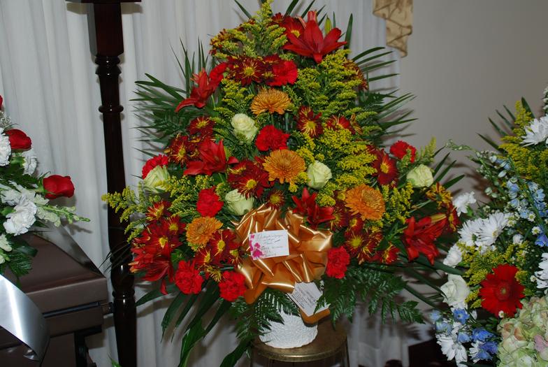Large red and orange floral arrangement with a gold bow in a white vase