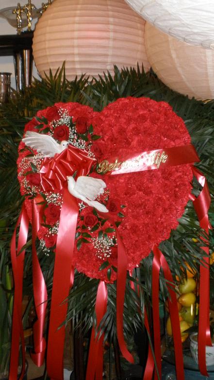 Heart-shaped red floral tribute with roses, ribbons, and white doves