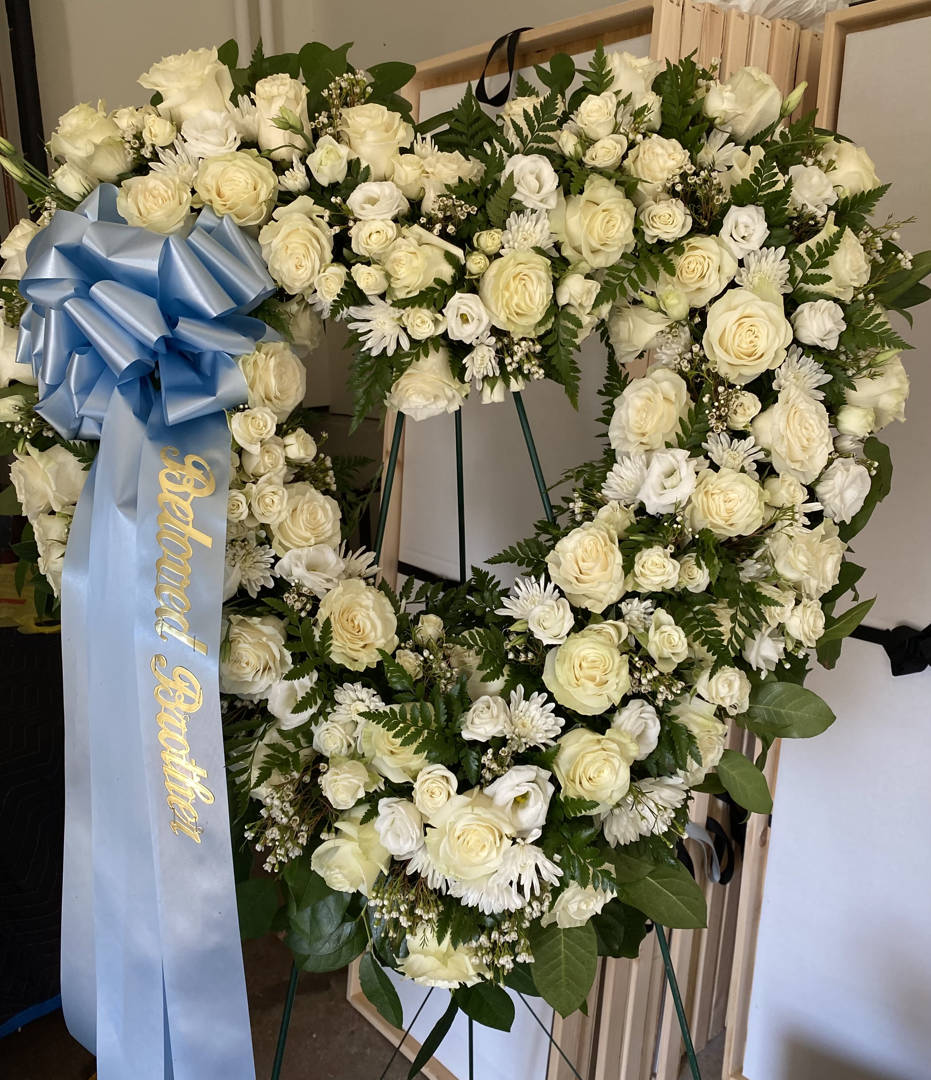 Large white floral funeral wreath with a blue ribbon on an easel