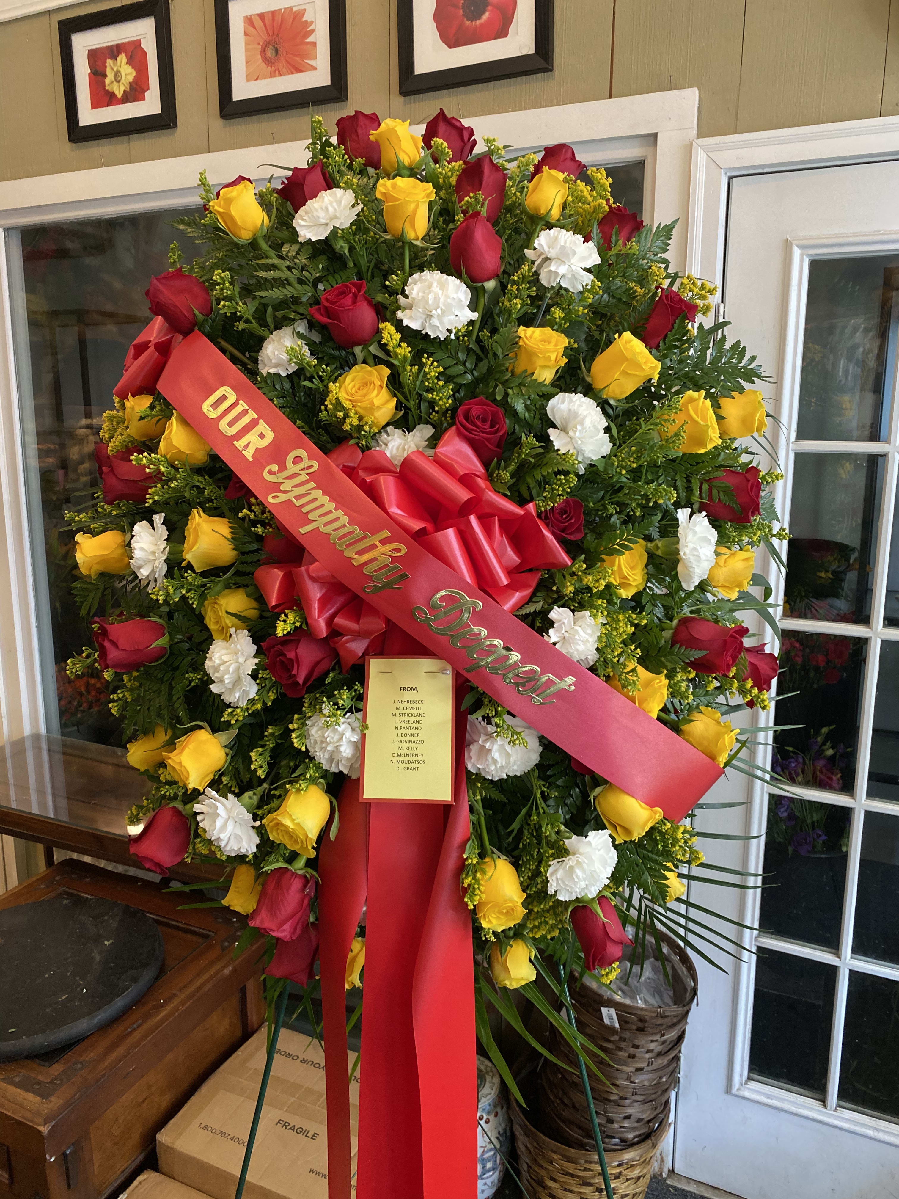 Large standing wreath of red, yellow, and white roses with a red ribbon