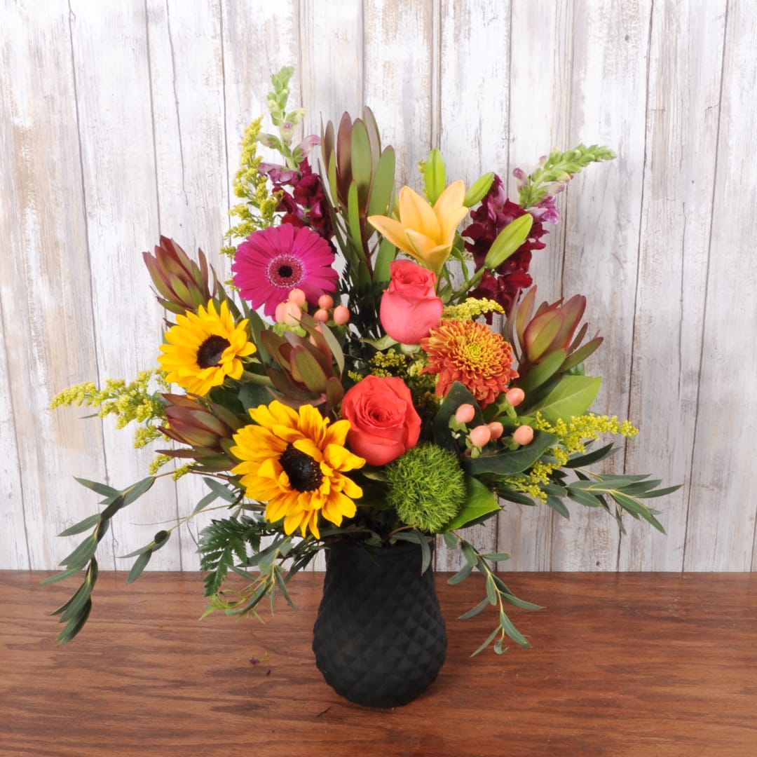 Mixed bouquet with sunflowers, roses, lilies, and a black vase