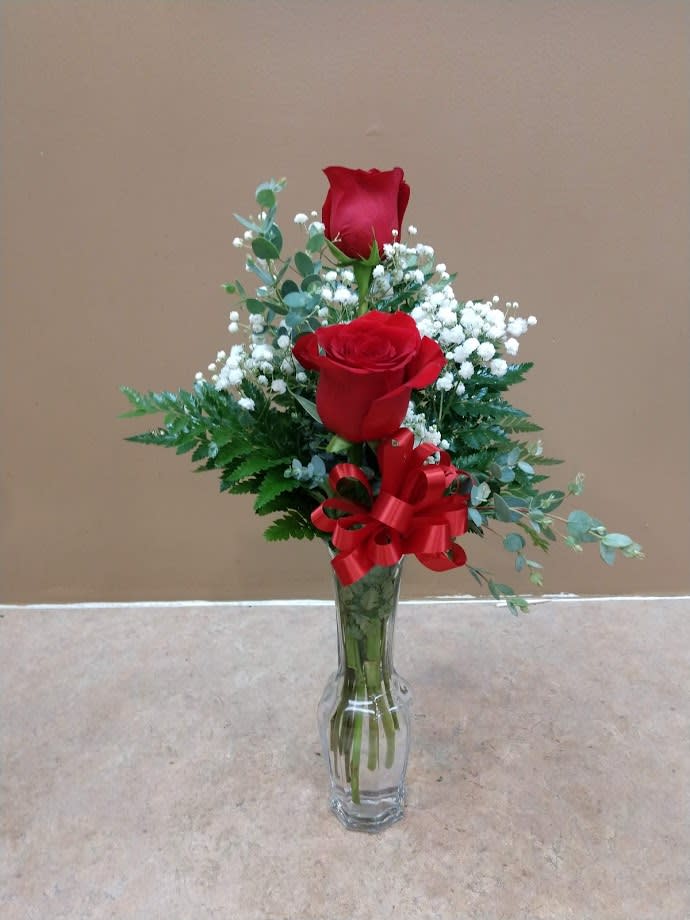 Two red roses in a clear glass vase with baby's breath and a red ribbon