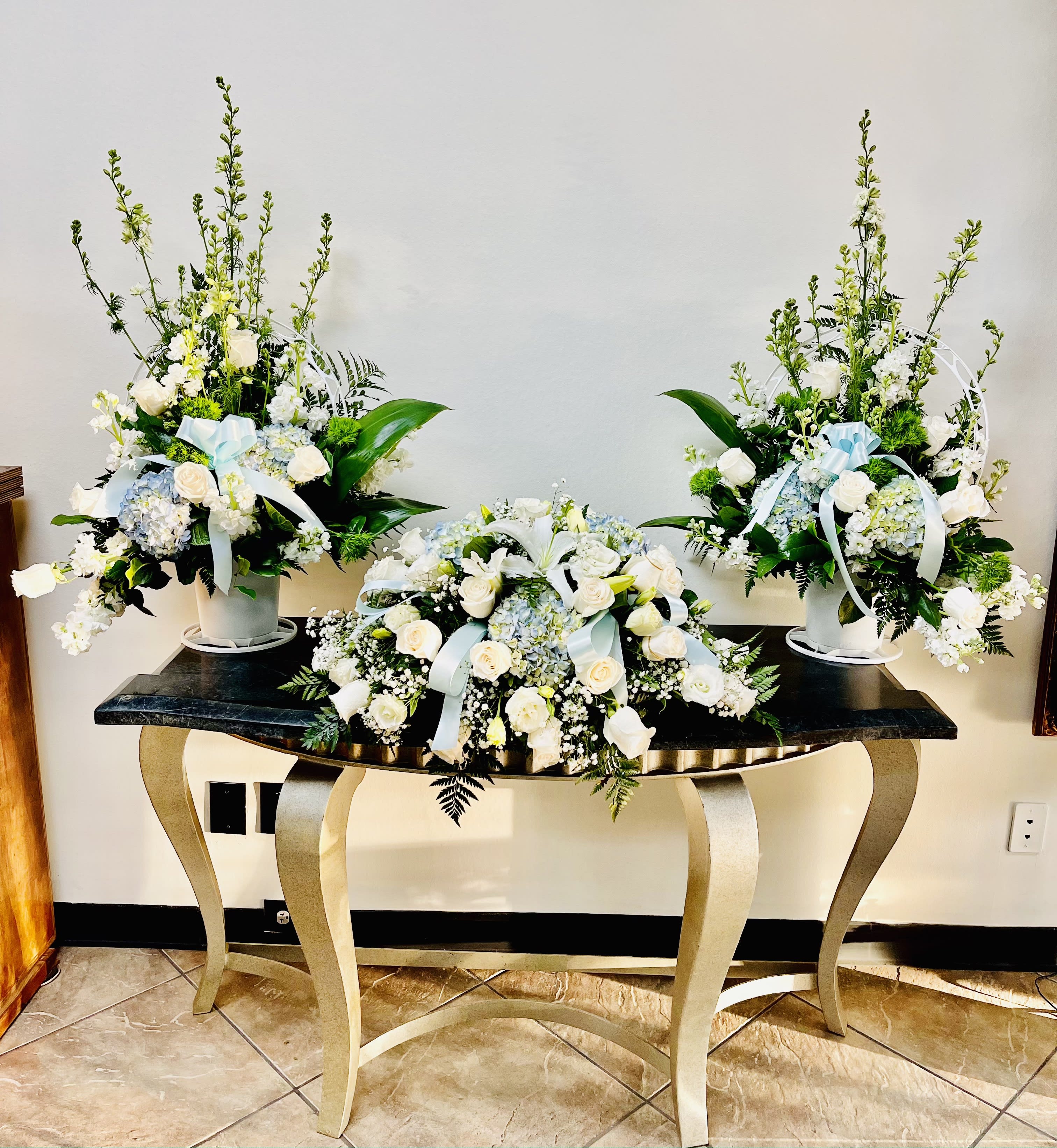 Three white floral arrangements with pale blue ribbons on a table
