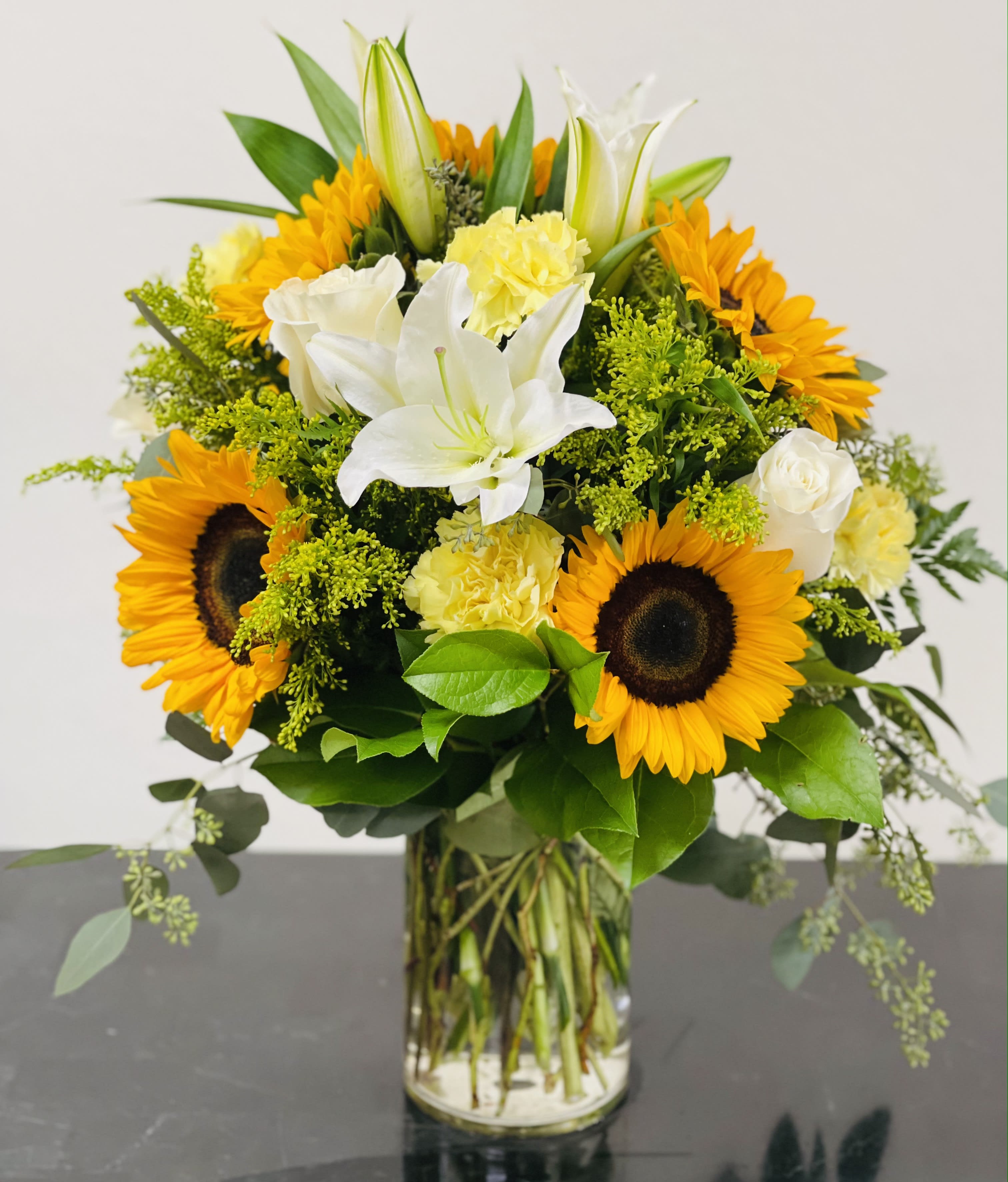 Bouquet of sunflowers, white lilies, and yellow carnations in a glass vase