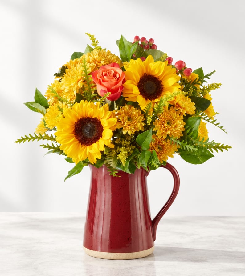 Sunflower and rose bouquet in a red ceramic pitcher