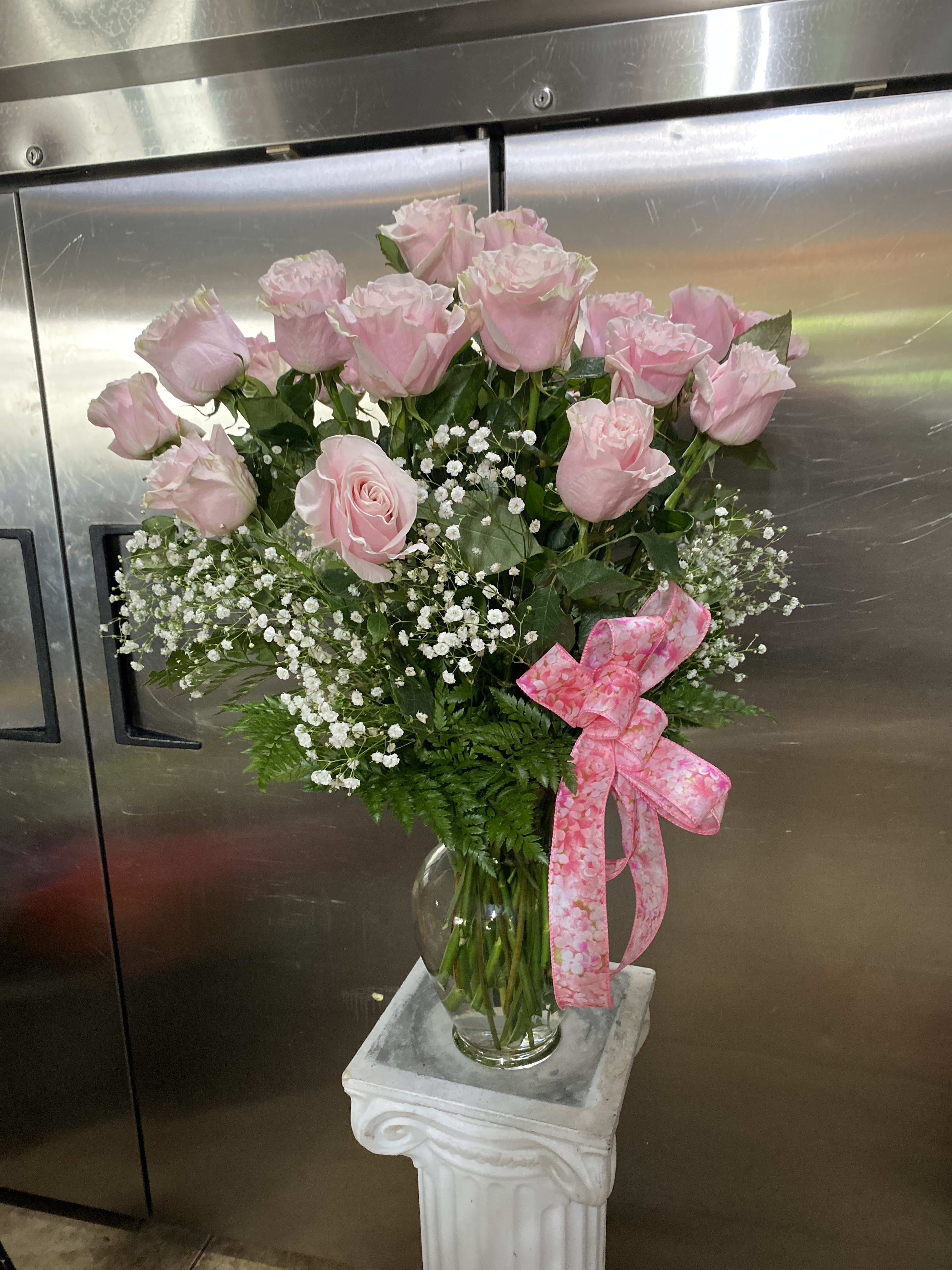 Pink roses in a glass vase with baby's breath and a pink ribbon