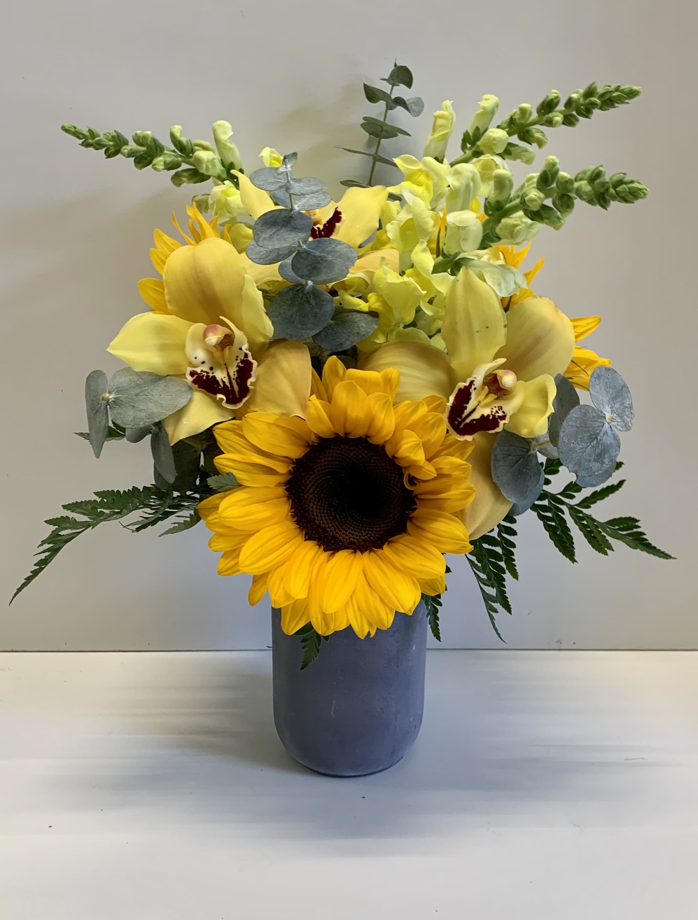 Sunflower and yellow orchid arrangement in a blue vase