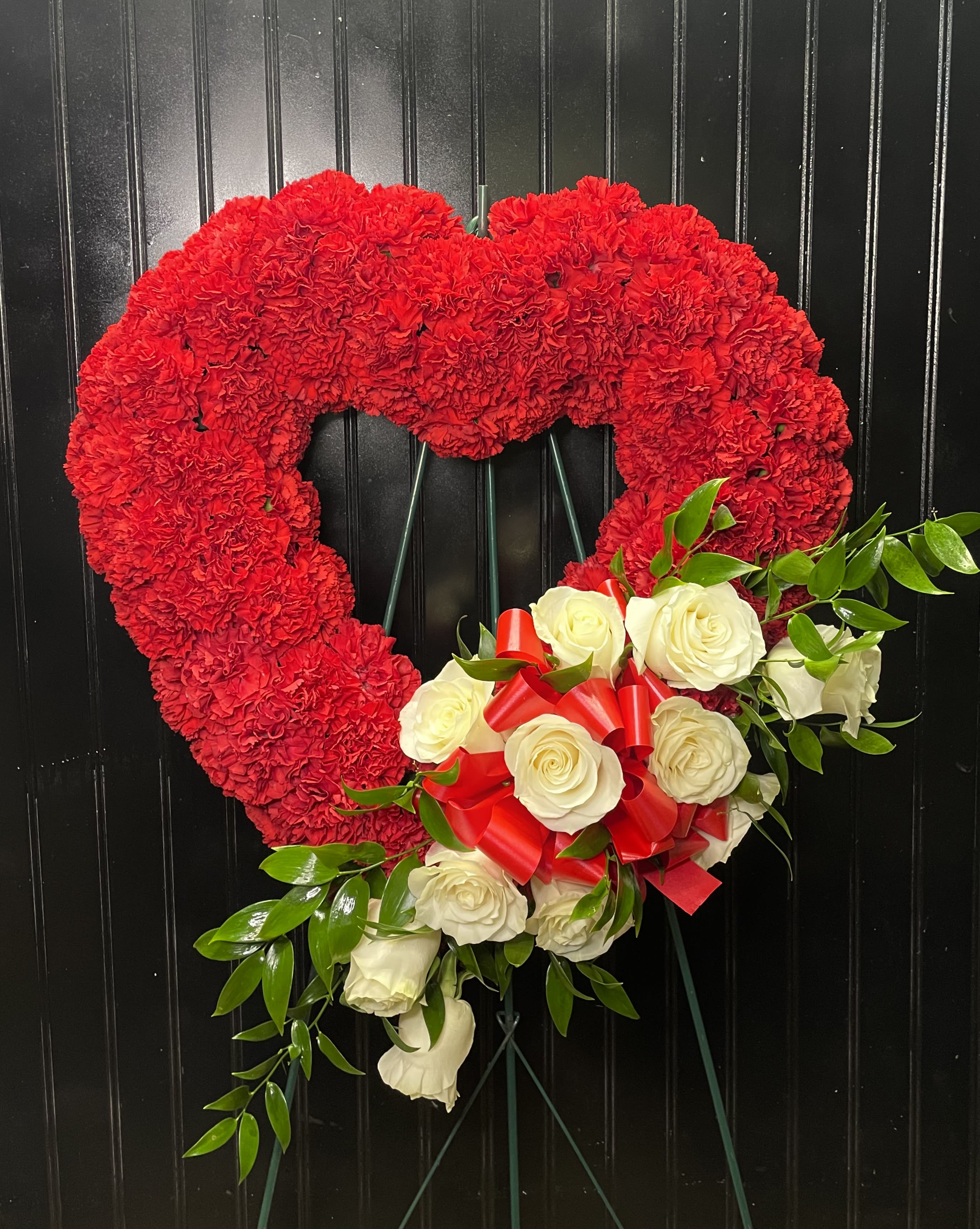 Heart-shaped red carnation wreath with white roses and a red ribbon bow