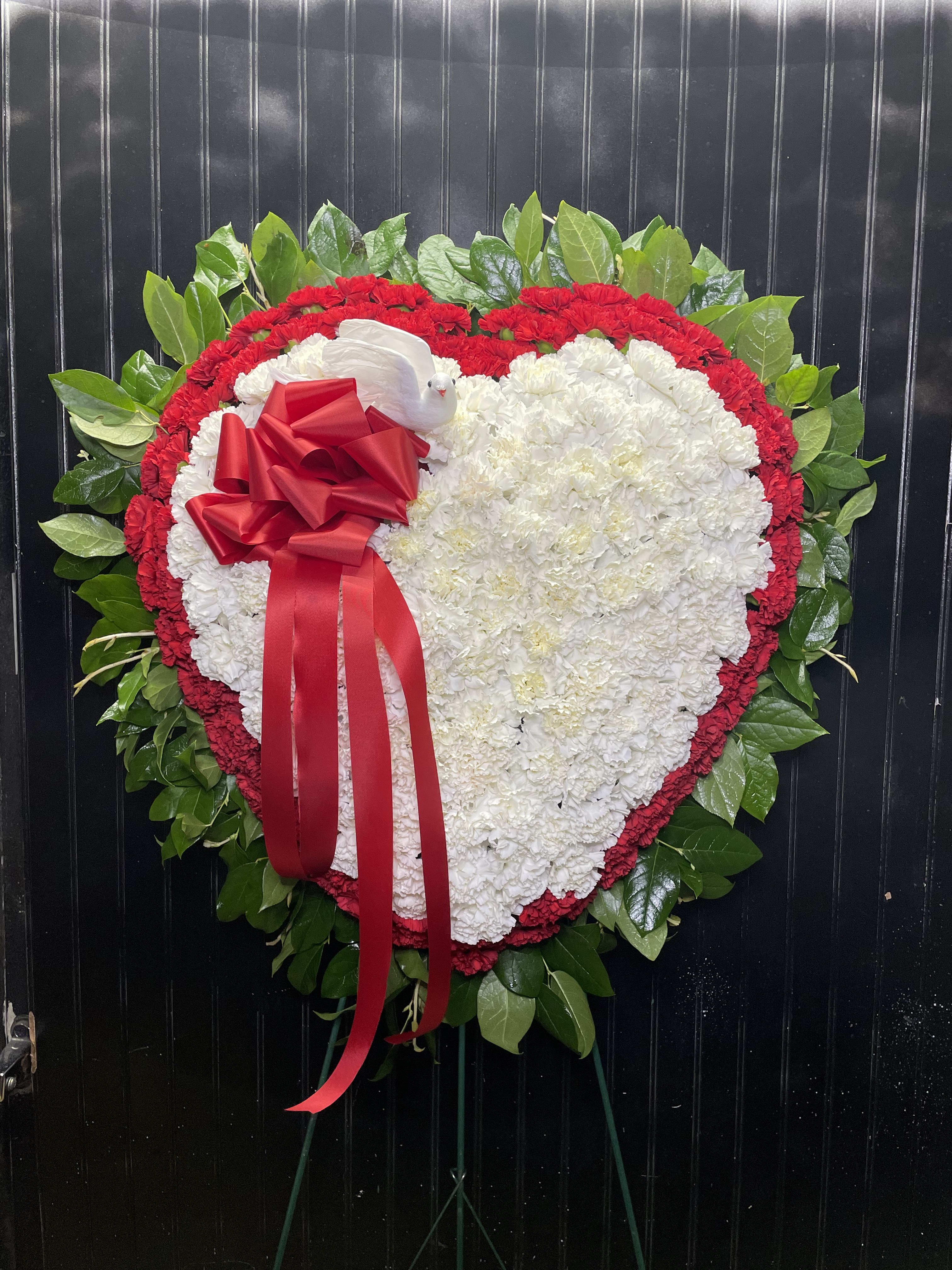 Heart-shaped floral wreath with white and red flowers and a red ribbon bow