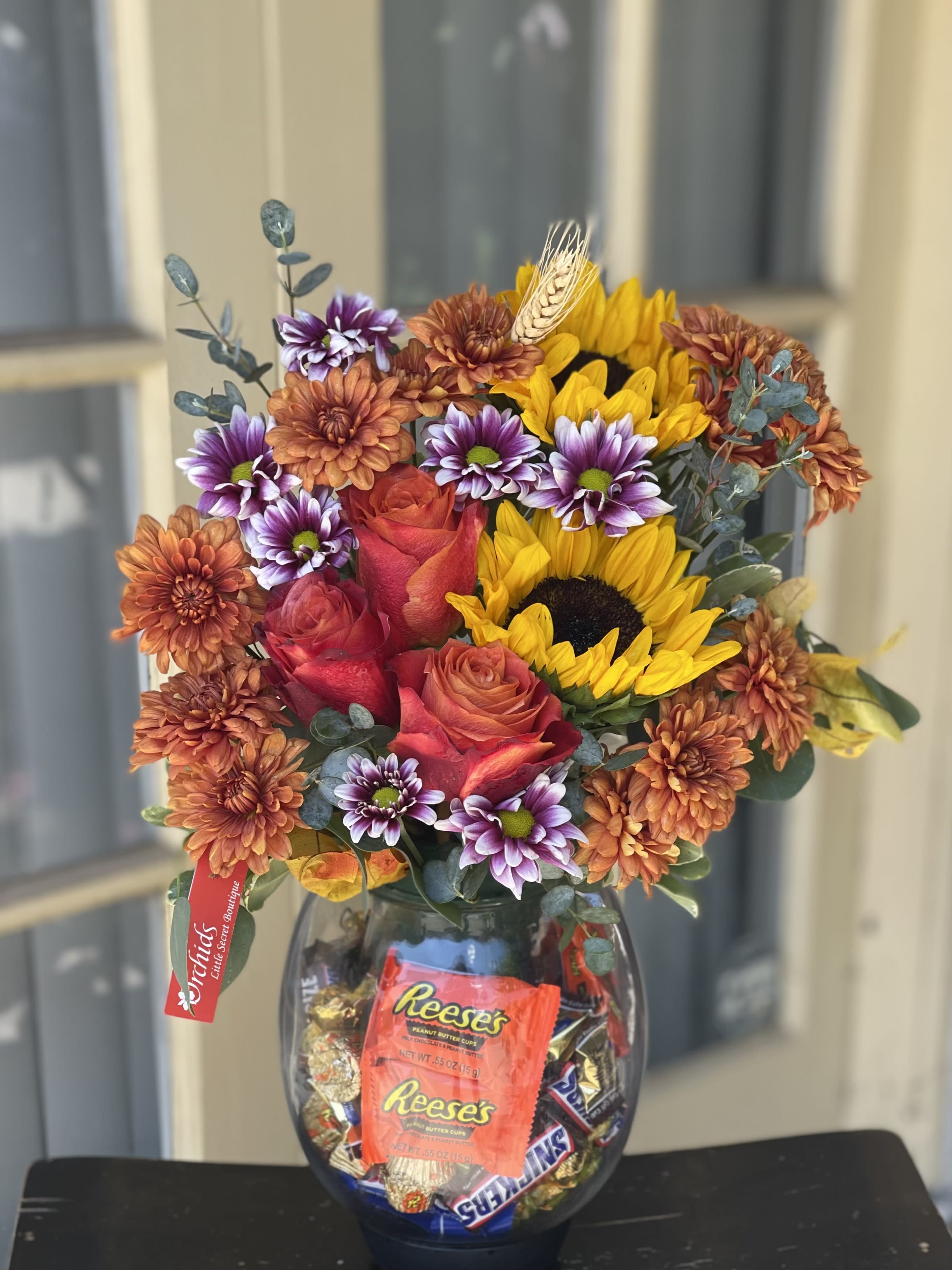 Mixed bouquet of roses, sunflowers, and chrysanthemums in a glass vase with candy