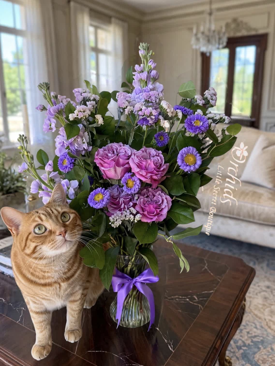 Purple bouquet in a glass vase beside an orange tabby cat