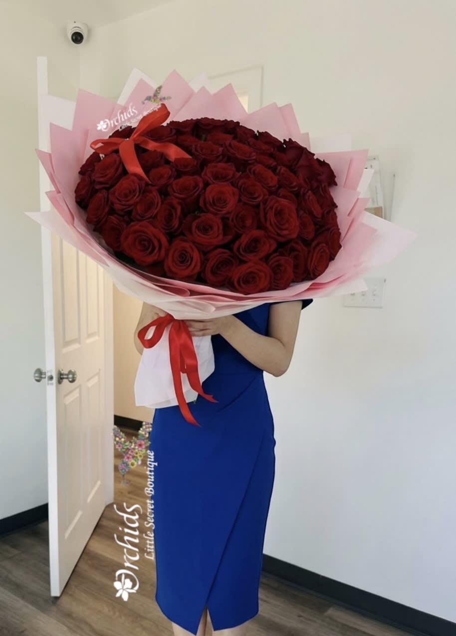 Large bouquet of red roses wrapped in pink paper with a red ribbon