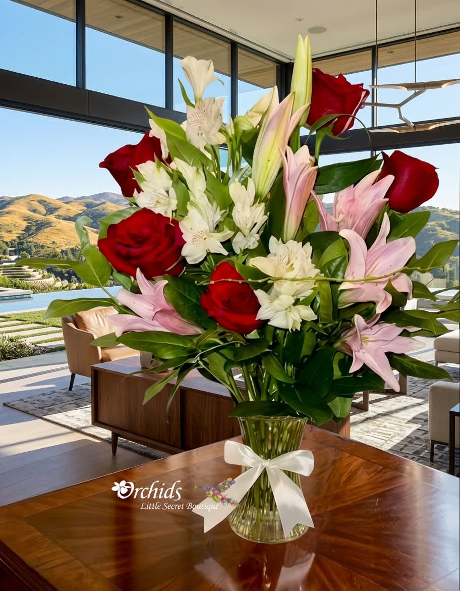 Bouquet of red roses, pink lilies, and white alstroemeria in a glass vase with a white ribbon