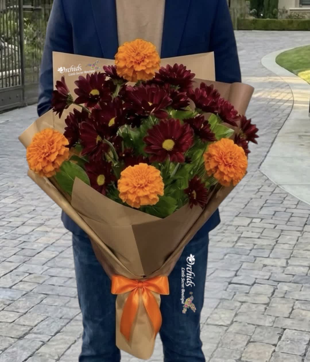Bouquet of burgundy daisies and orange marigolds wrapped in brown paper