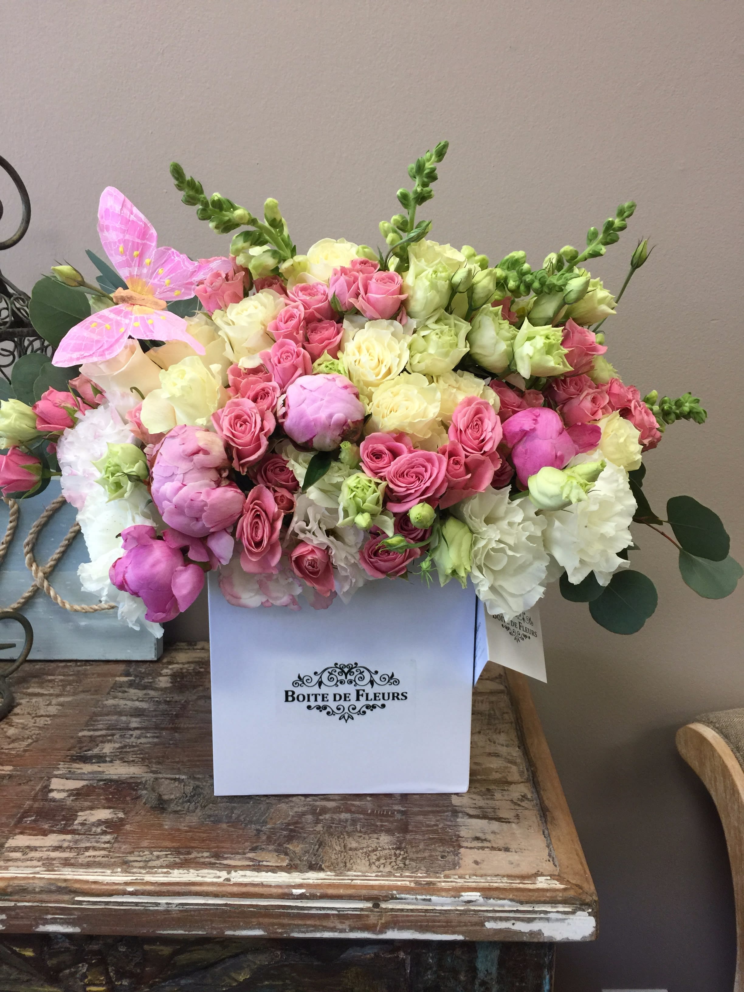 Pink and cream roses arranged in a white box with a pink butterfly accent.