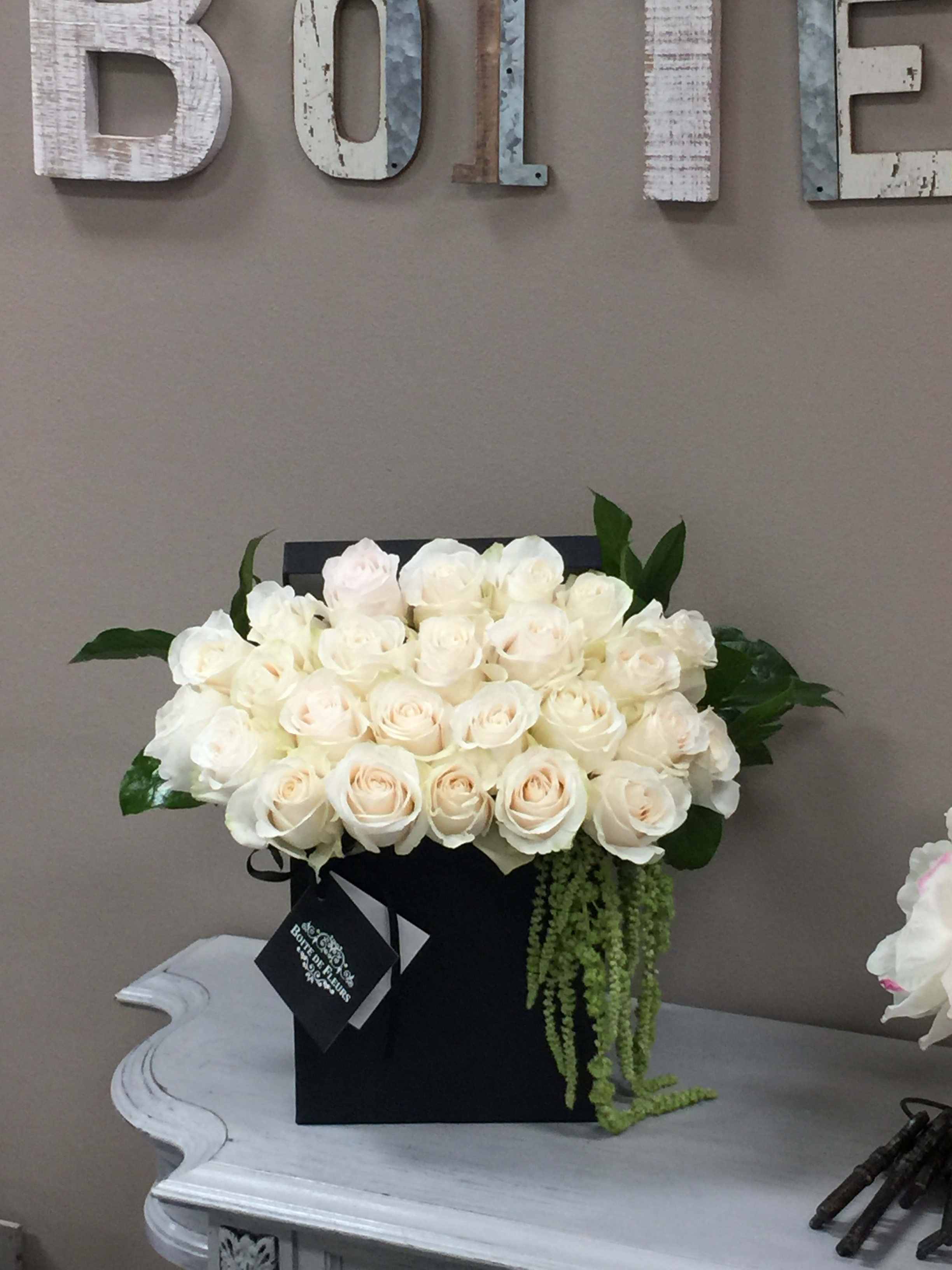 Cream rose arrangement in a black box with trailing greenery