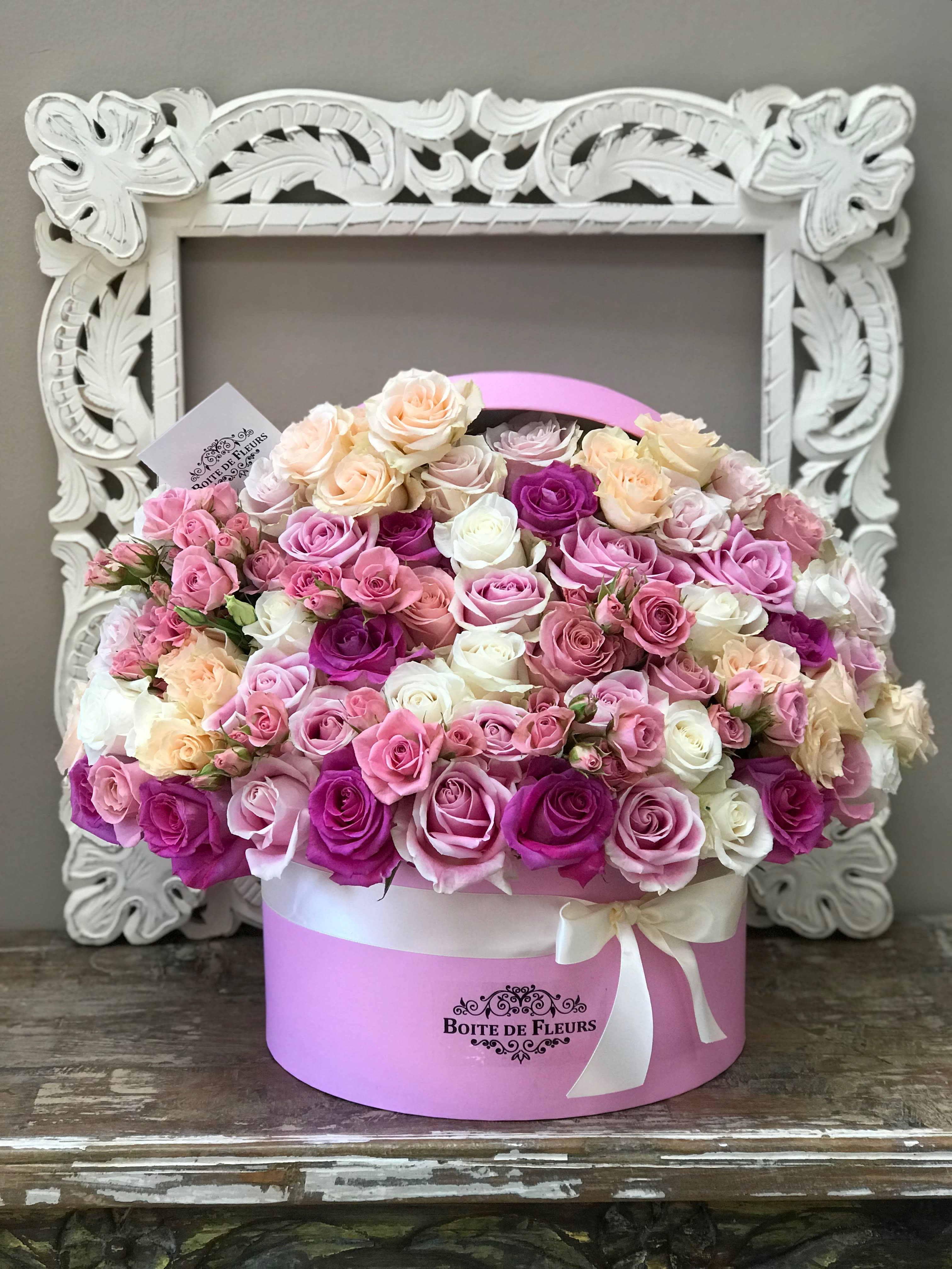 Pink and cream roses arranged in a round hat box with a ribbon