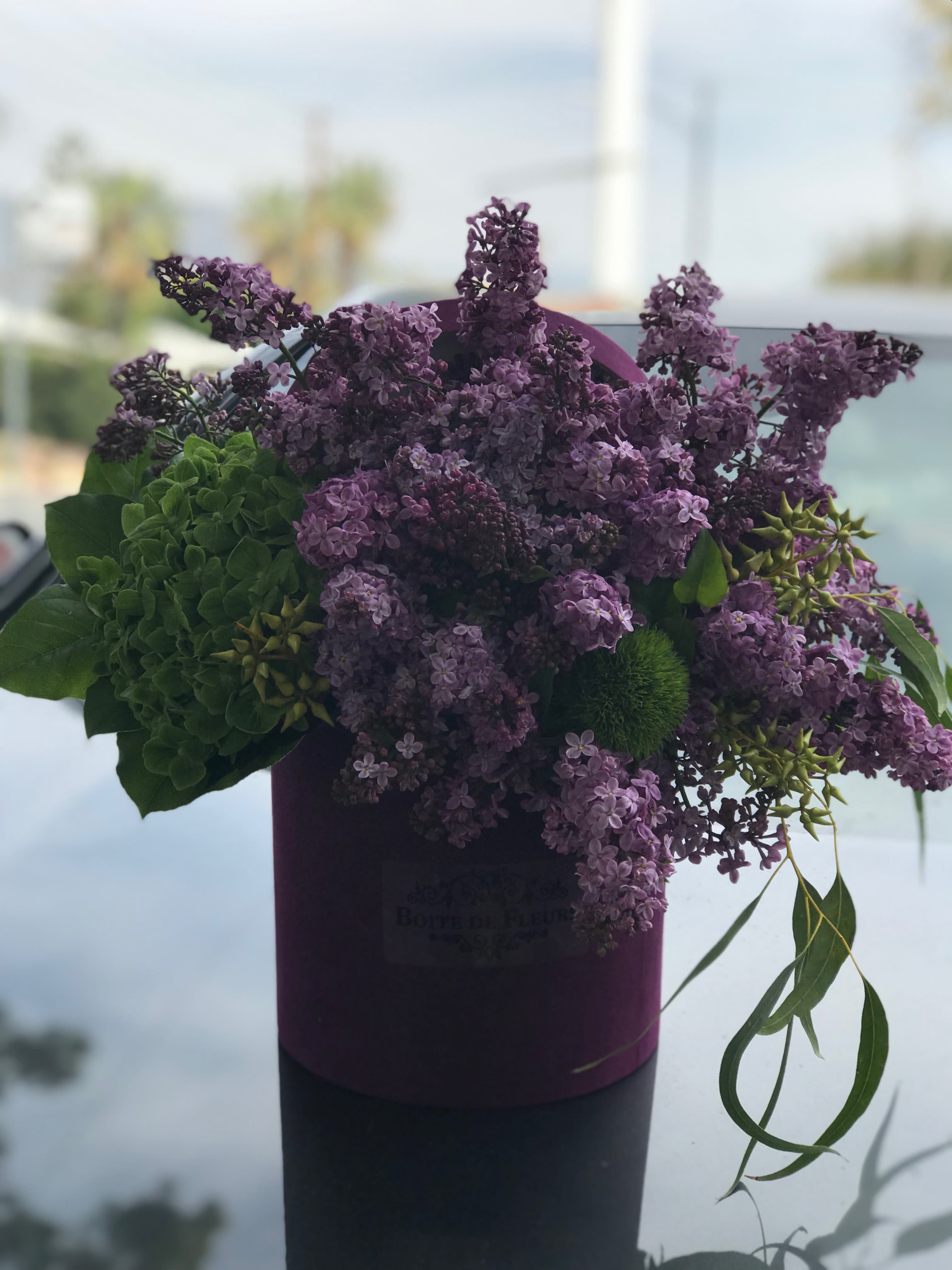 Purple lilac bouquet in a dark cylindrical box with green accents