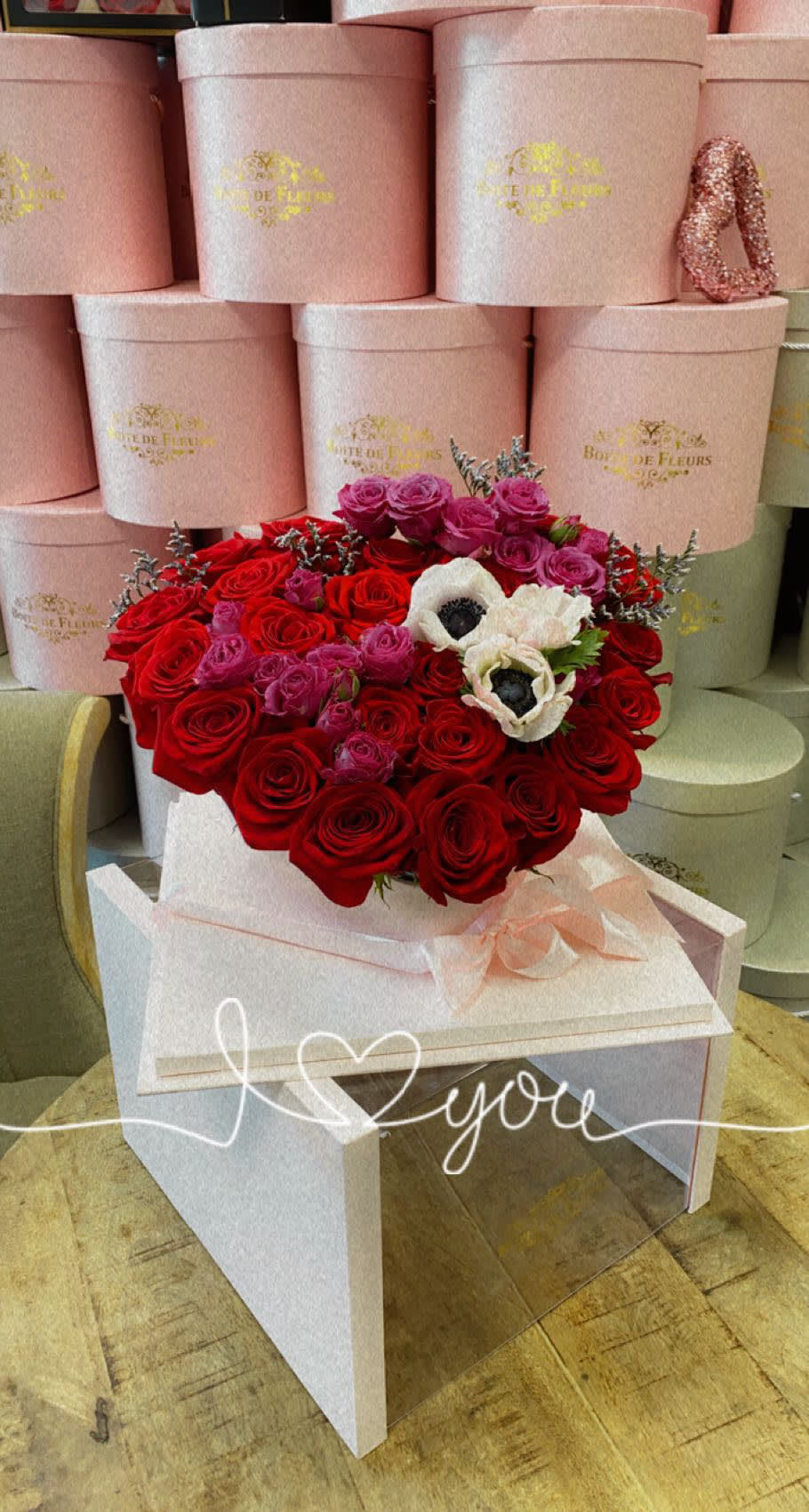 Heart-shaped bouquet of red and pink roses with white flowers in a pink box