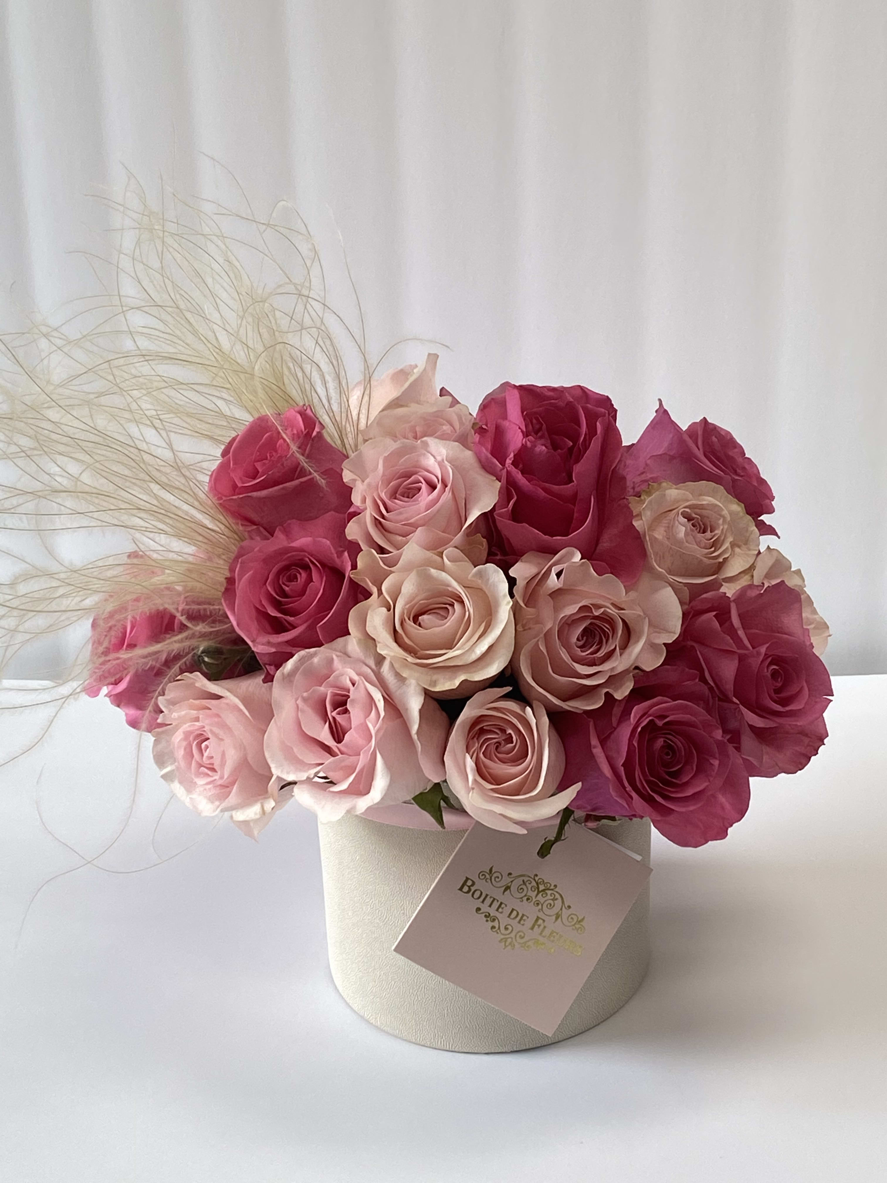 Pink and blush roses arranged in a round box with decorative grass