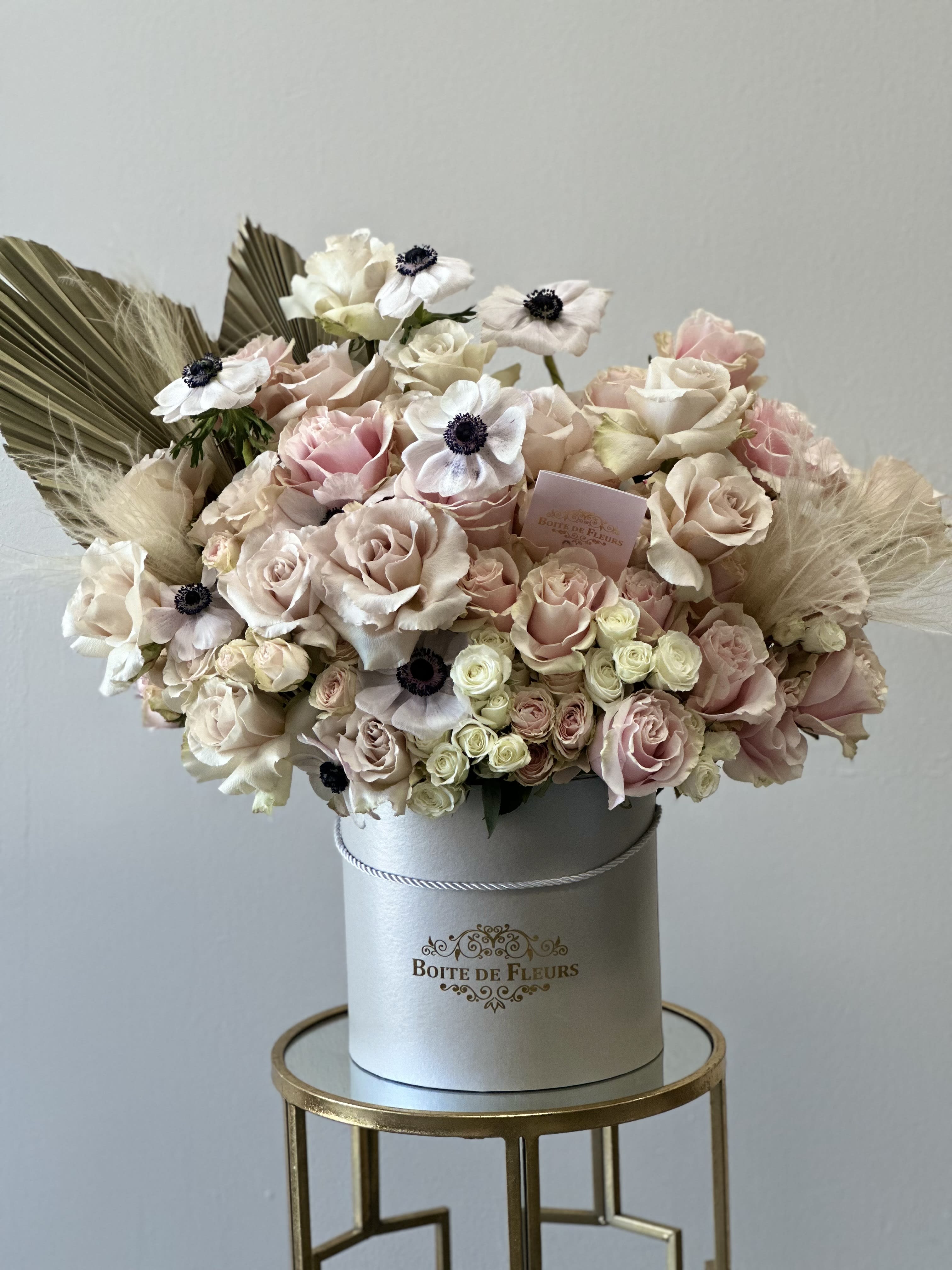 Blush and cream roses arranged in a round hatbox with dried accents