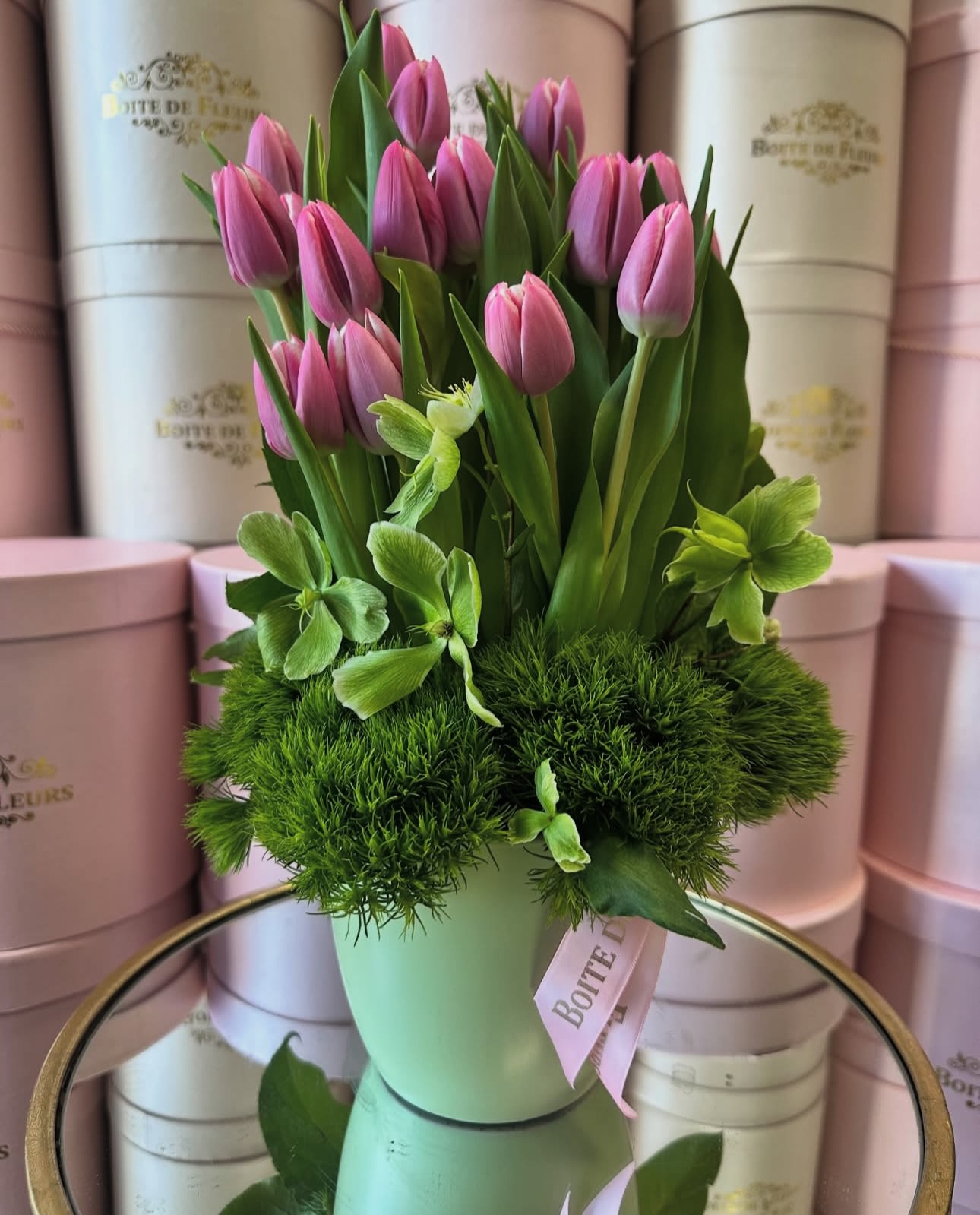 Pink tulips arranged in a pale green vase with green blooms