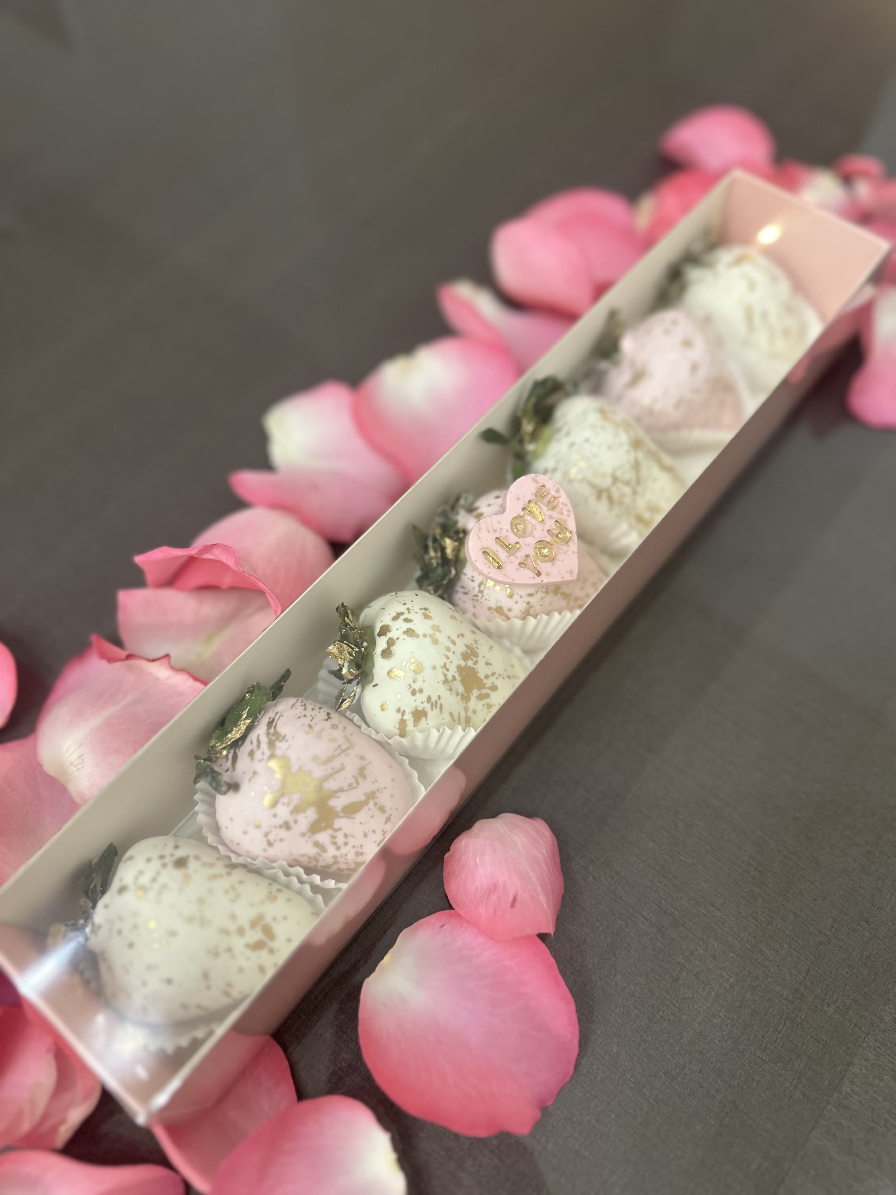 Box of pastel chocolate-covered strawberries with pink rose petals