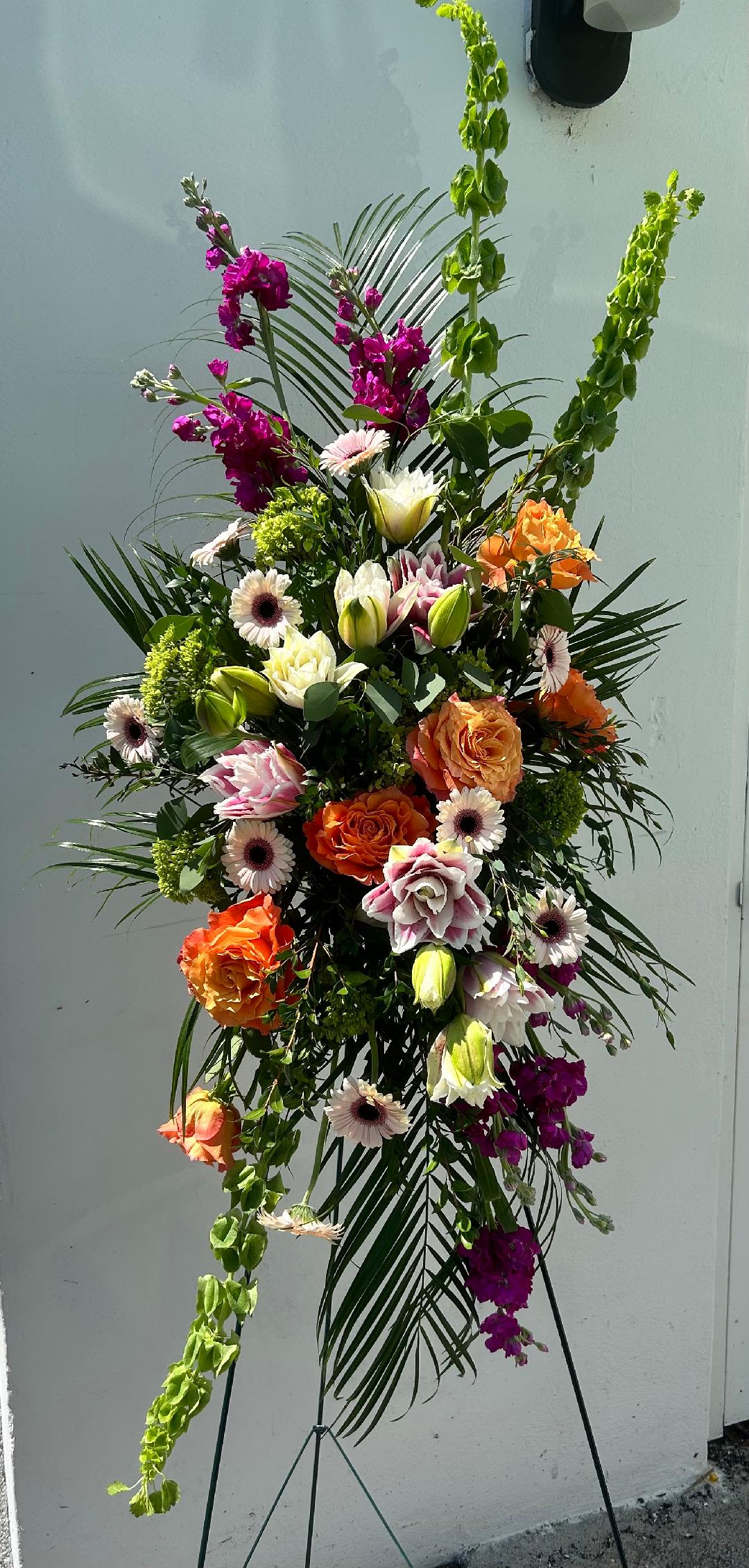 CFS147 - Standing Spray for a funeral service is vibrant tones made with spring flowers such as lilies, roses, gerbera daises, stock and other blooms. 