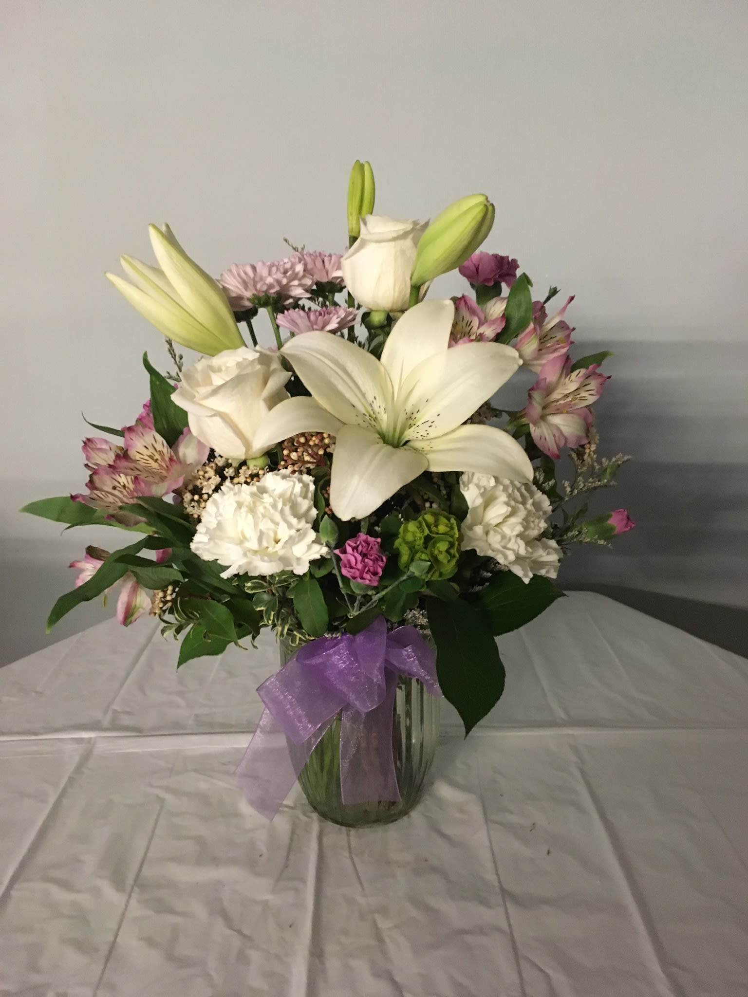 Bouquet of white lilies and pink flowers in a glass vase with a purple ribbon