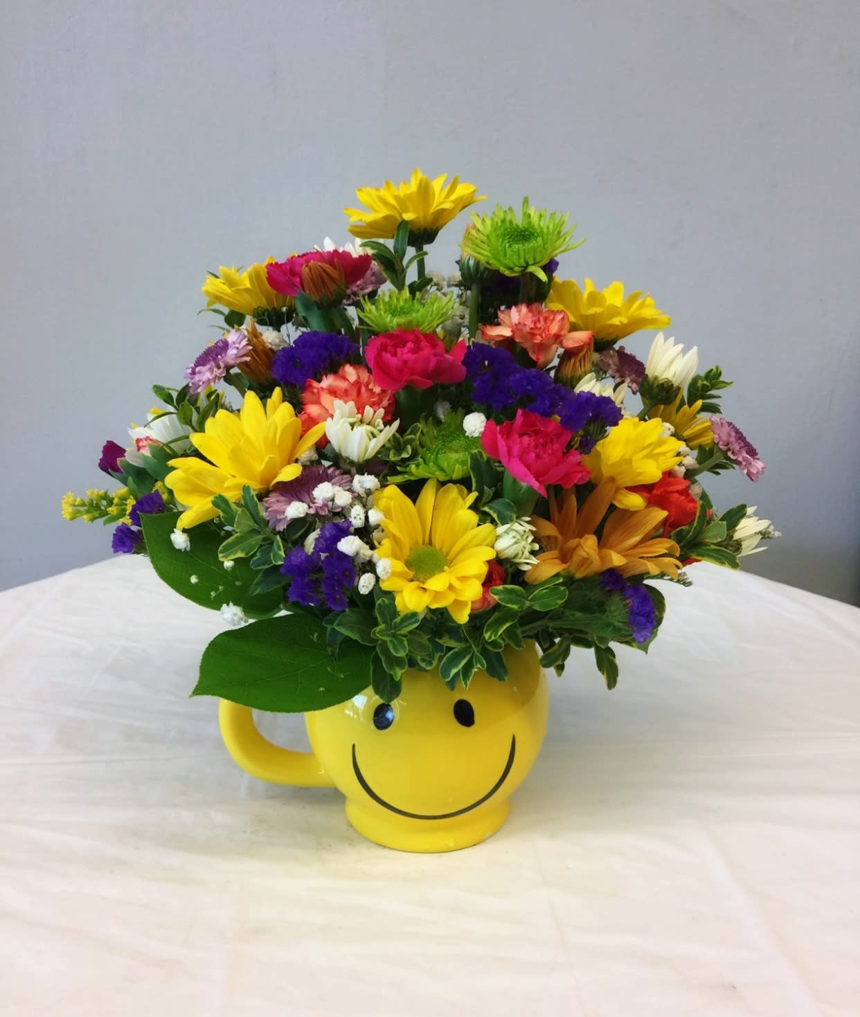 Colorful mixed flower arrangement in a yellow smiley-face mug