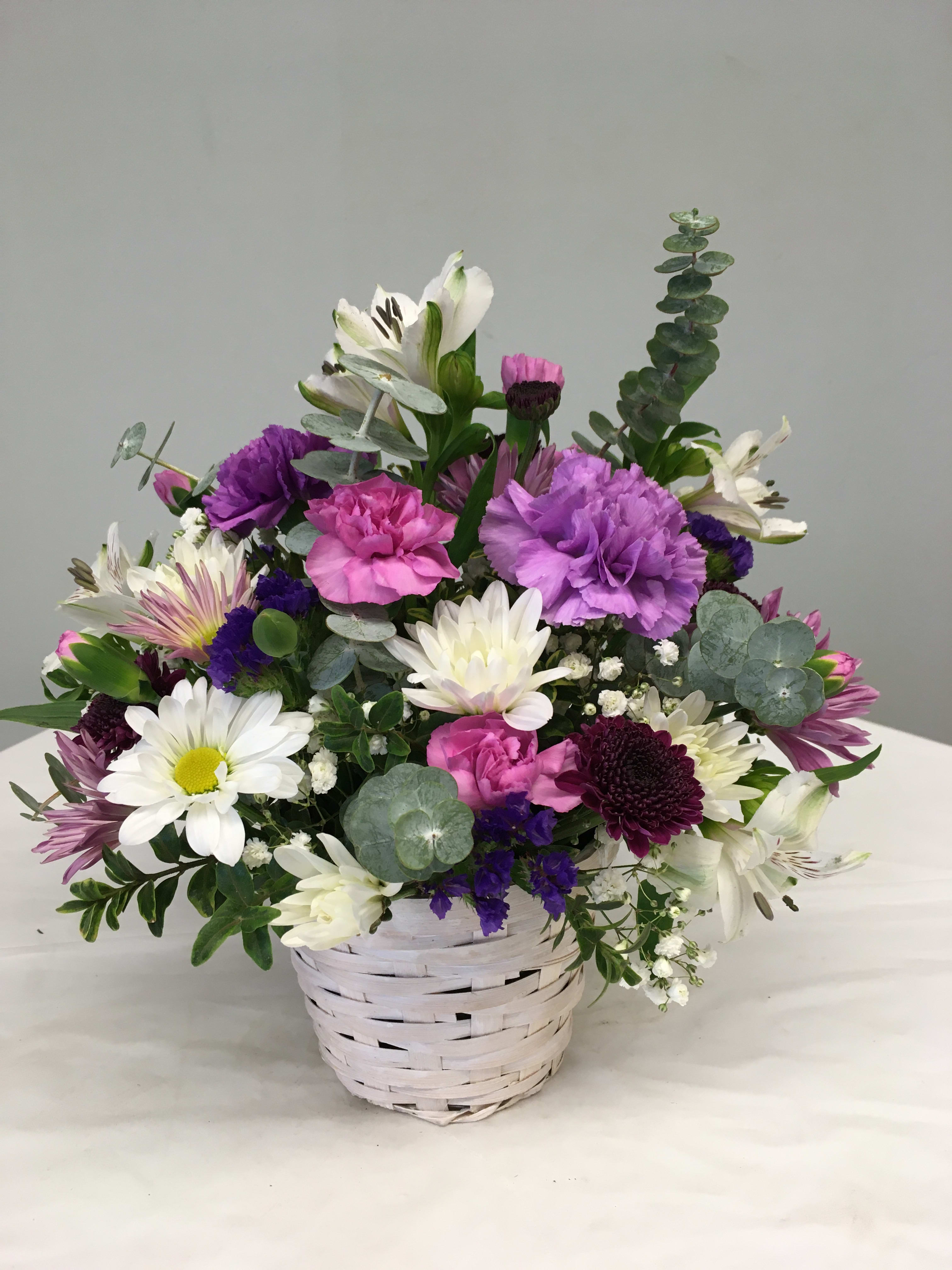 Mixed bouquet of white, pink, and purple flowers in a white basket
