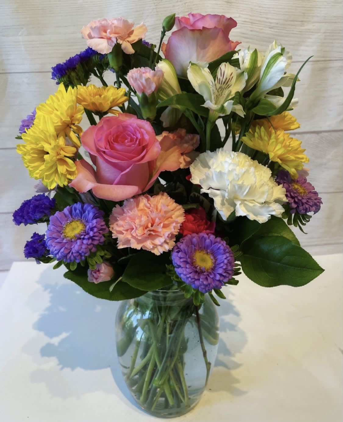 Mixed bouquet of pink, yellow, purple, and white flowers in a glass vase