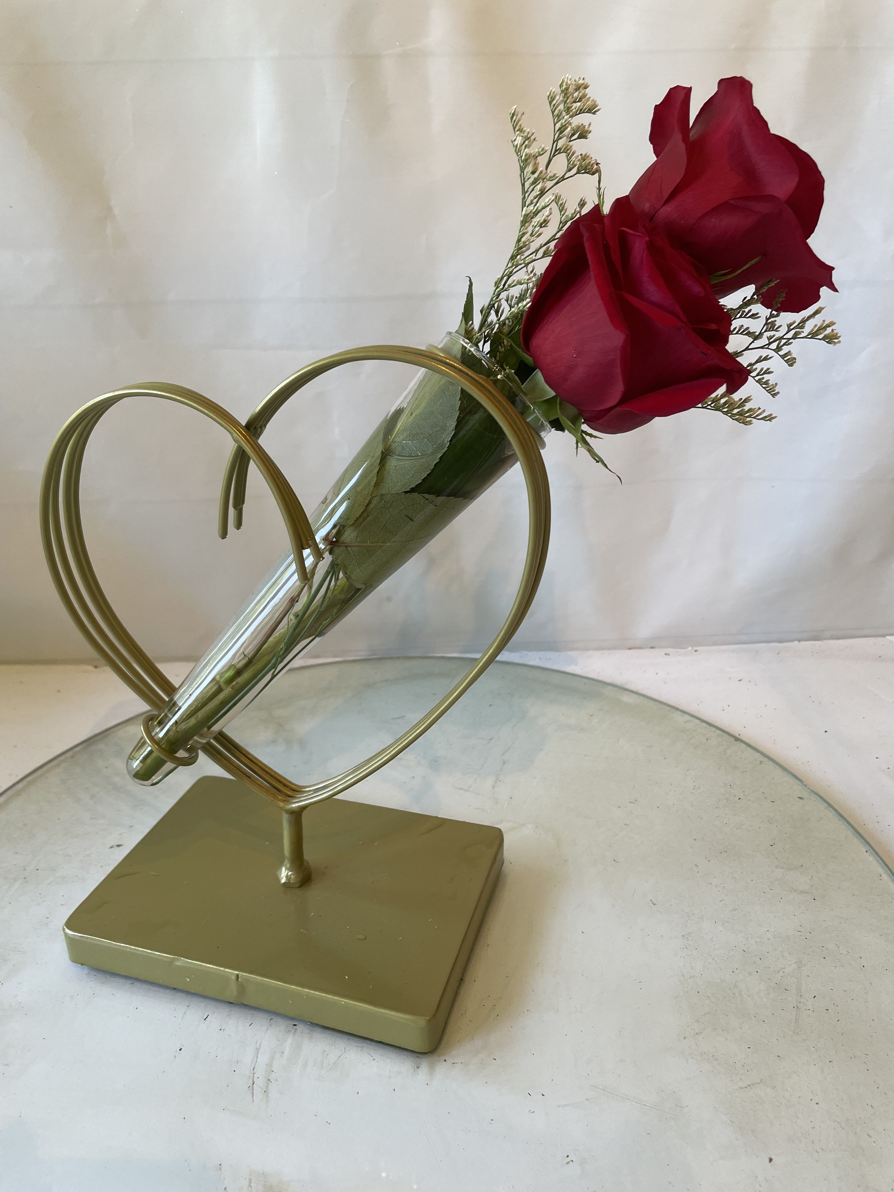 Two red roses in a clear cone vase on a gold heart stand