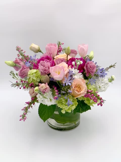 Low glass vase arrangement with pink tulips, roses, hydrangeas, and other pastel flowers