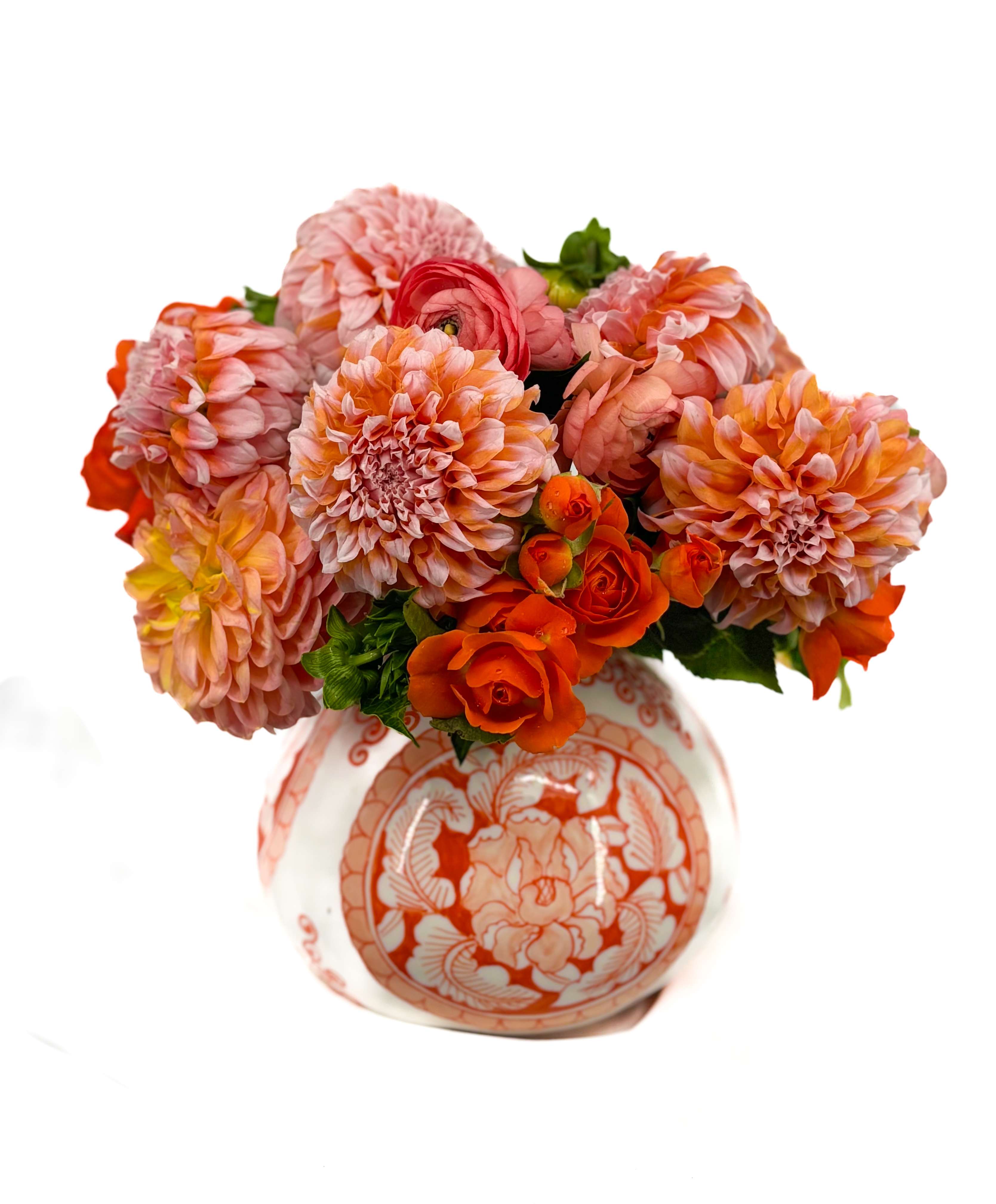 Round arrangement of orange and pink dahlias and roses in a patterned ceramic vase