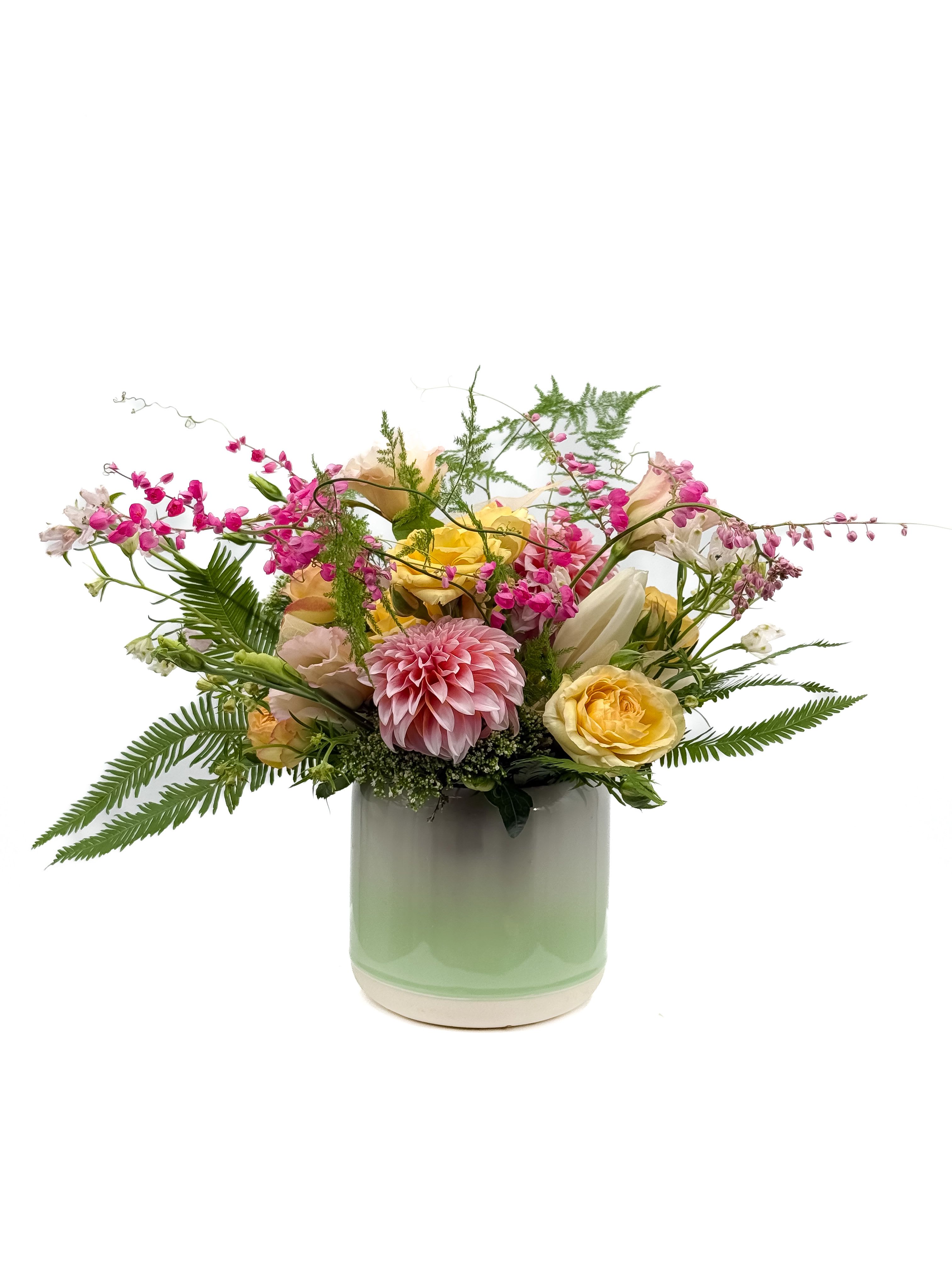 Courtney - This joyful bouquet dances with soft pink dahlias, sunny yellow roses, and trailing pink blossoms—all nestled among airy ferns and dreamy greenery. Set in a fresh mint ombré ceramic vase, it captures the feeling of stumbling upon a hidden garden in full bloom. Perfect for celebrations, sweet surprises, or anyone who loves a touch of wild beauty.