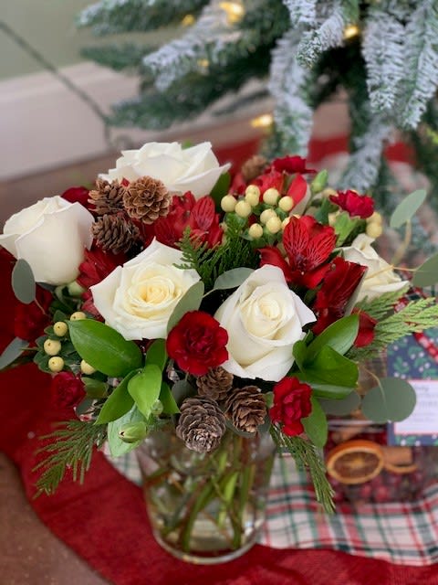 Red and white rose bouquet with pinecones in a glass vase