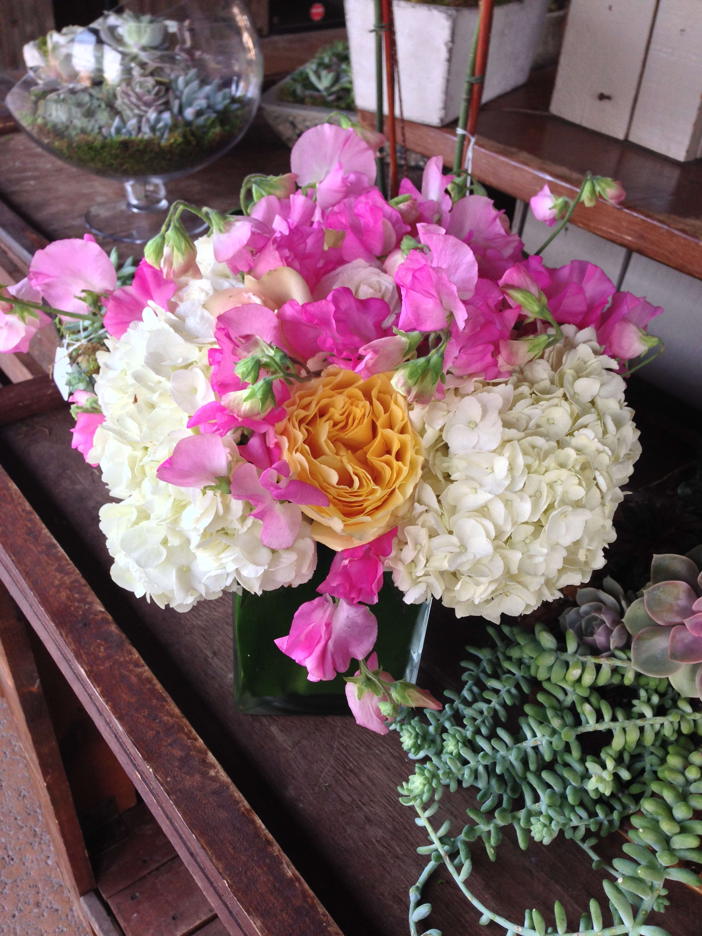 Pink sweet peas and white hydrangeas around a yellow rose in a glass vase
