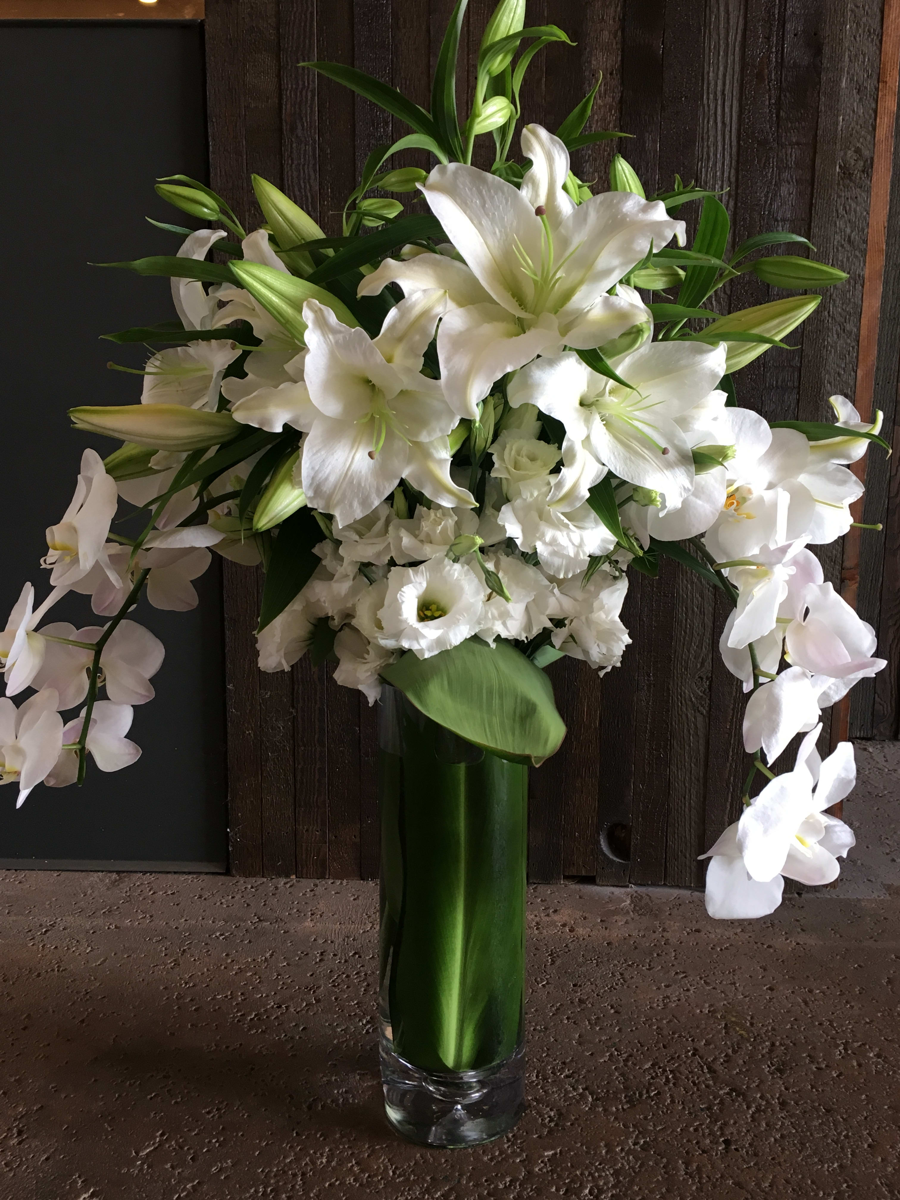White lilies and orchids arranged in a tall glass vase